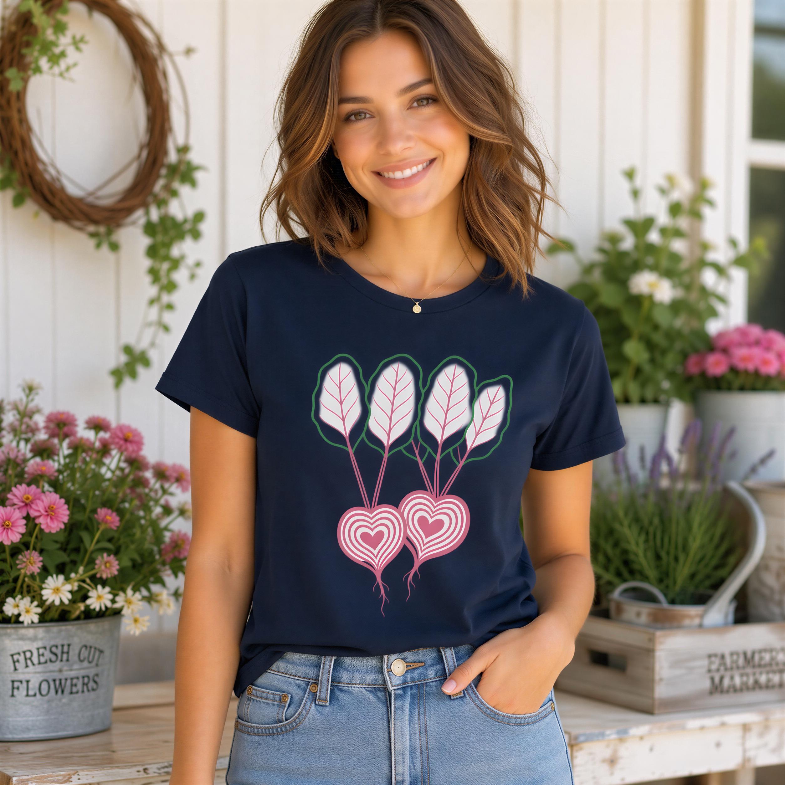 A woman wearing a navy blue t-shirt with a graphic of pink and white flowers stands in front of a white wall with a wreath and potted plants.