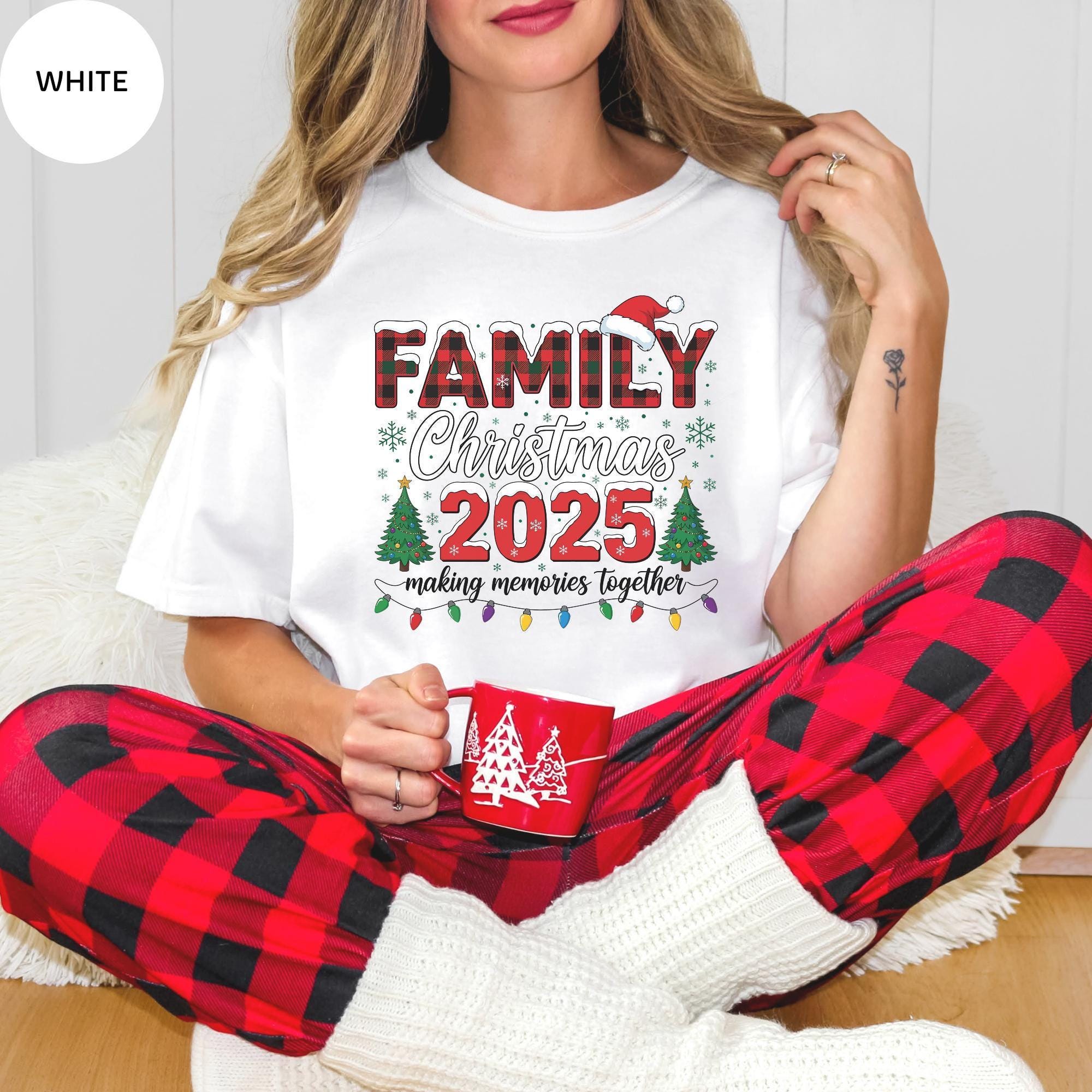 A woman wearing a white t-shirt with a Christmas-themed design and red plaid pajama bottoms, holding a red mug.