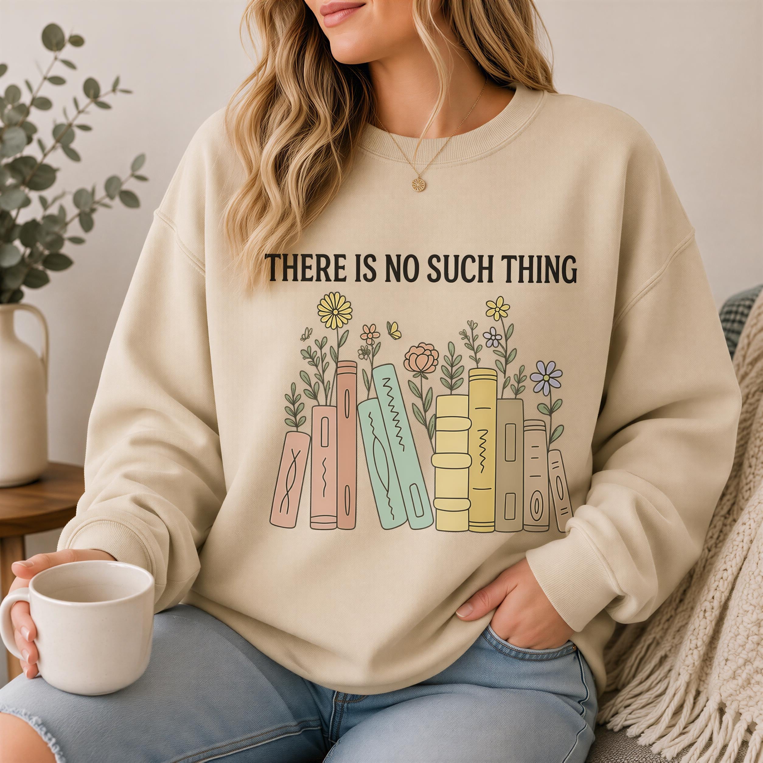A woman wearing a beige sweatshirt with a graphic design of colorful books and flowers, holding a coffee mug and sitting on a couch.