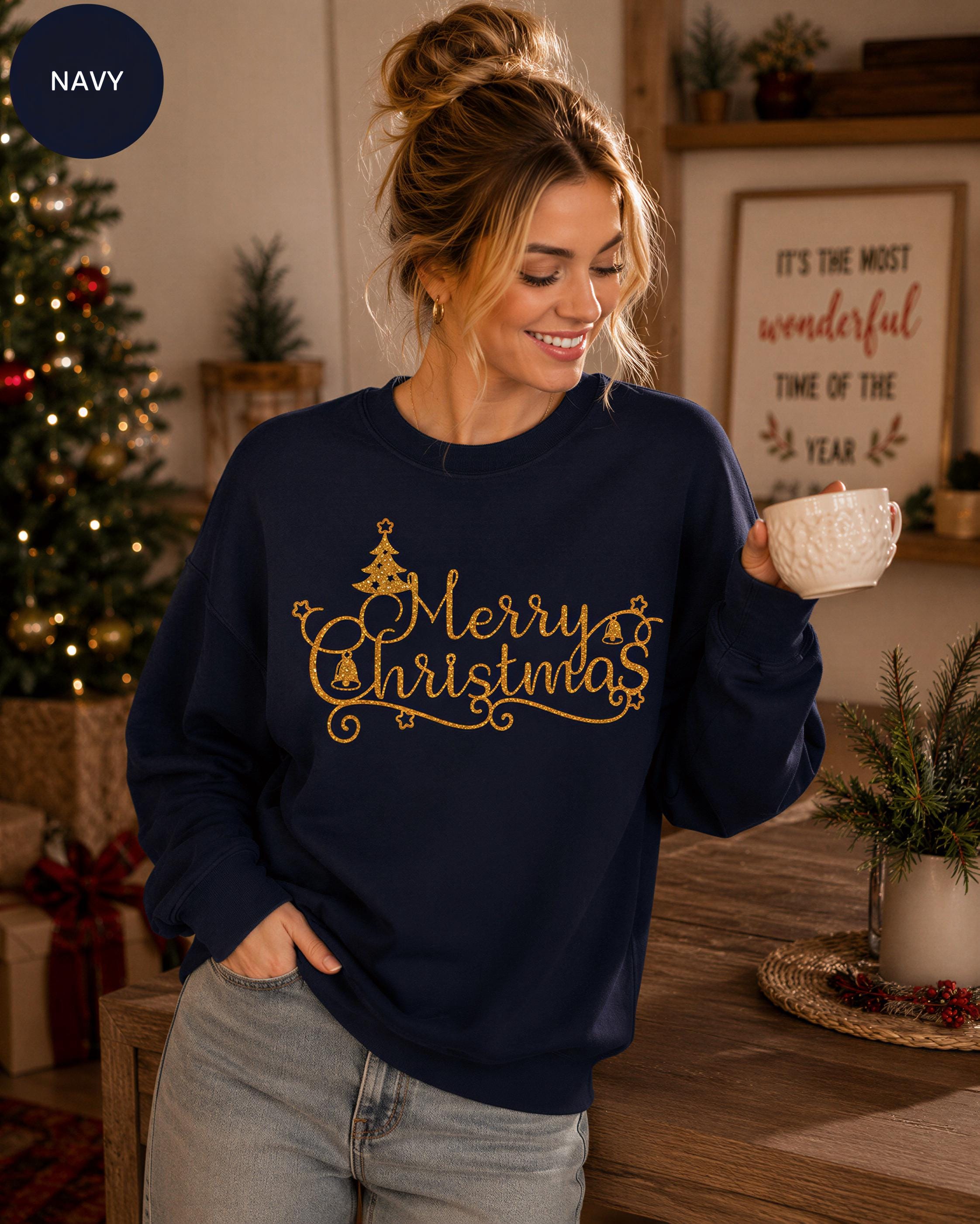 A woman wearing a navy blue sweatshirt with the text "Merry Christmas" is smiling and holding a white mug, with a Christmas tree and other holiday decorations visible in the background.