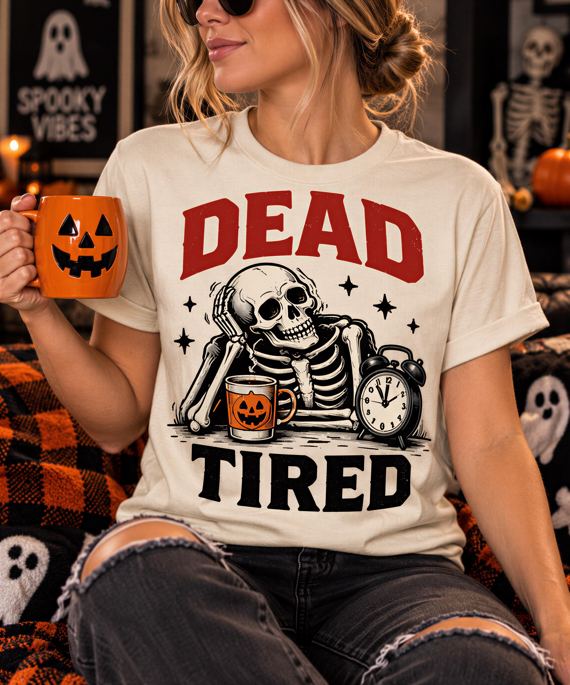 A woman wearing a white t-shirt with a graphic design of a skeleton holding a cup and a clock, with the text "DEAD TIRED" printed on it. She is sitting on a couch with a pumpkin-themed mug in her hand.
