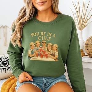 A woman wearing a green sweatshirt with a graphic design of a group of people enjoying drinks at a table.
