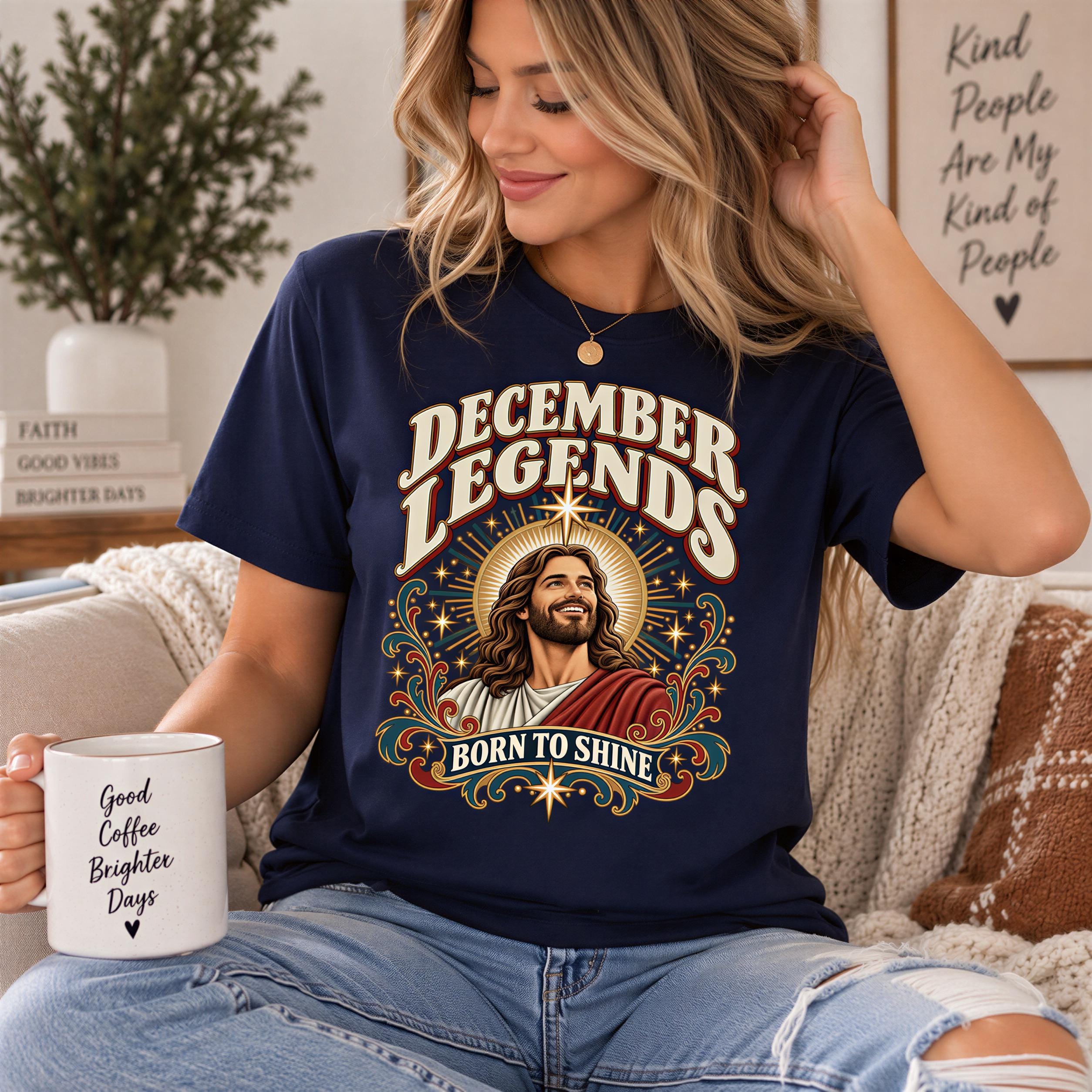 A woman wearing a navy blue t-shirt with a graphic design of a man's face and the text "December Legends Born to Shine" is sitting on a couch, holding a coffee mug.
