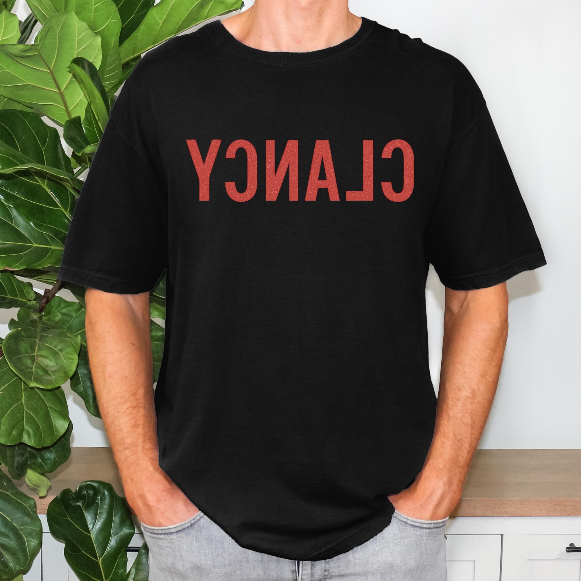 A person wearing a black t-shirt with the word "CLAN" printed on it.