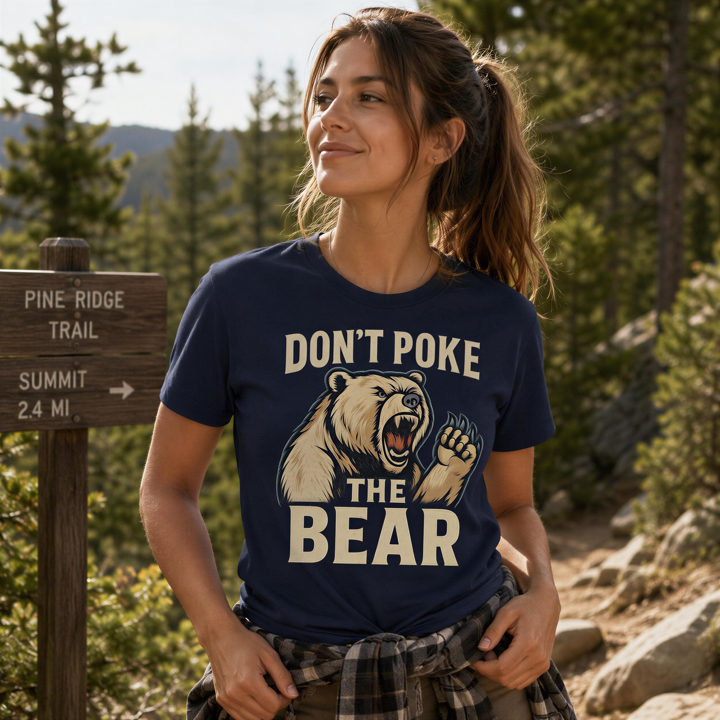 A woman wearing a blue t-shirt with a graphic of a bear and the text "DON'T POKER THE BEAR" standing in a forested area.