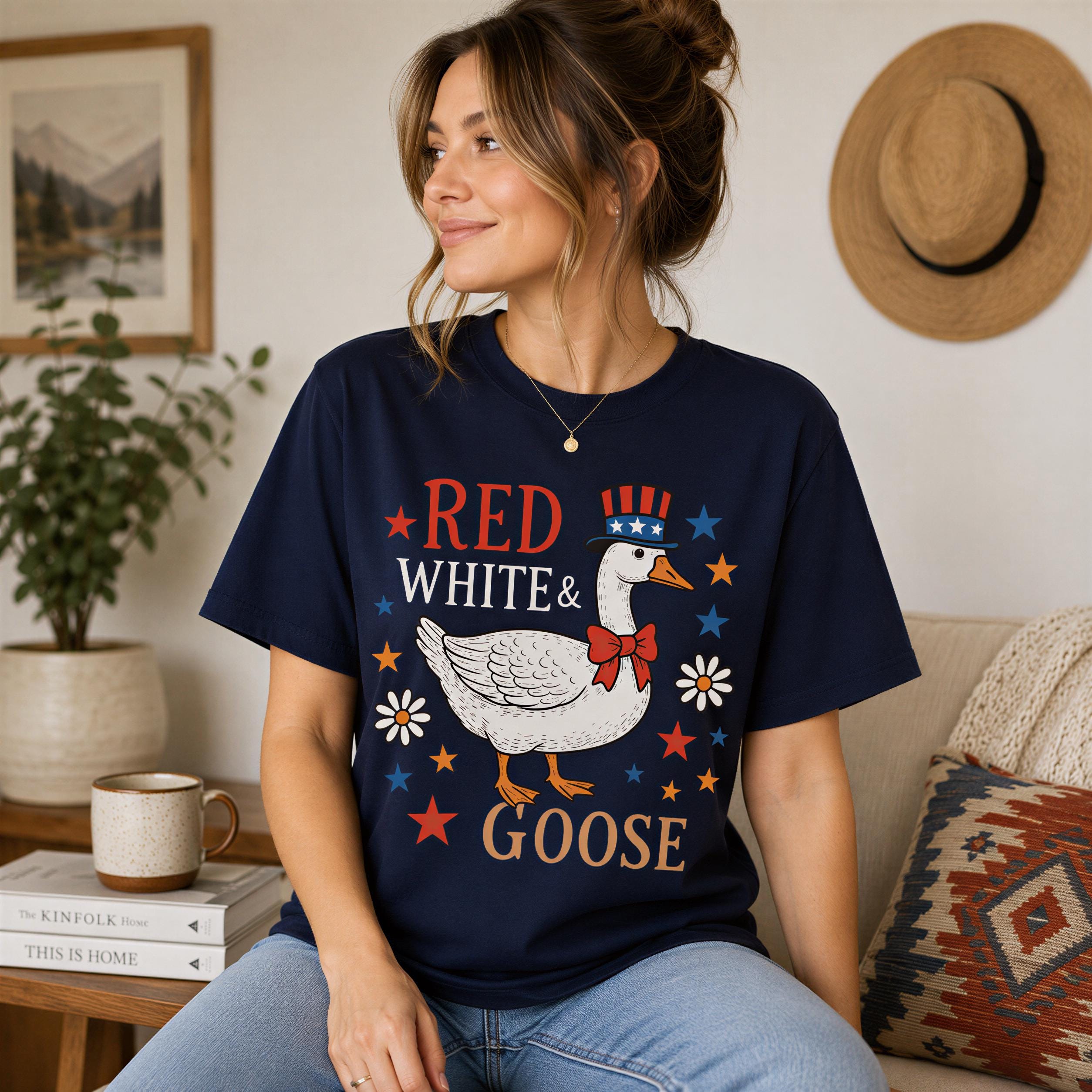 A woman wearing a navy blue t-shirt with a graphic of a goose and the text "RED WHITE & GOOSE" is sitting on a couch.