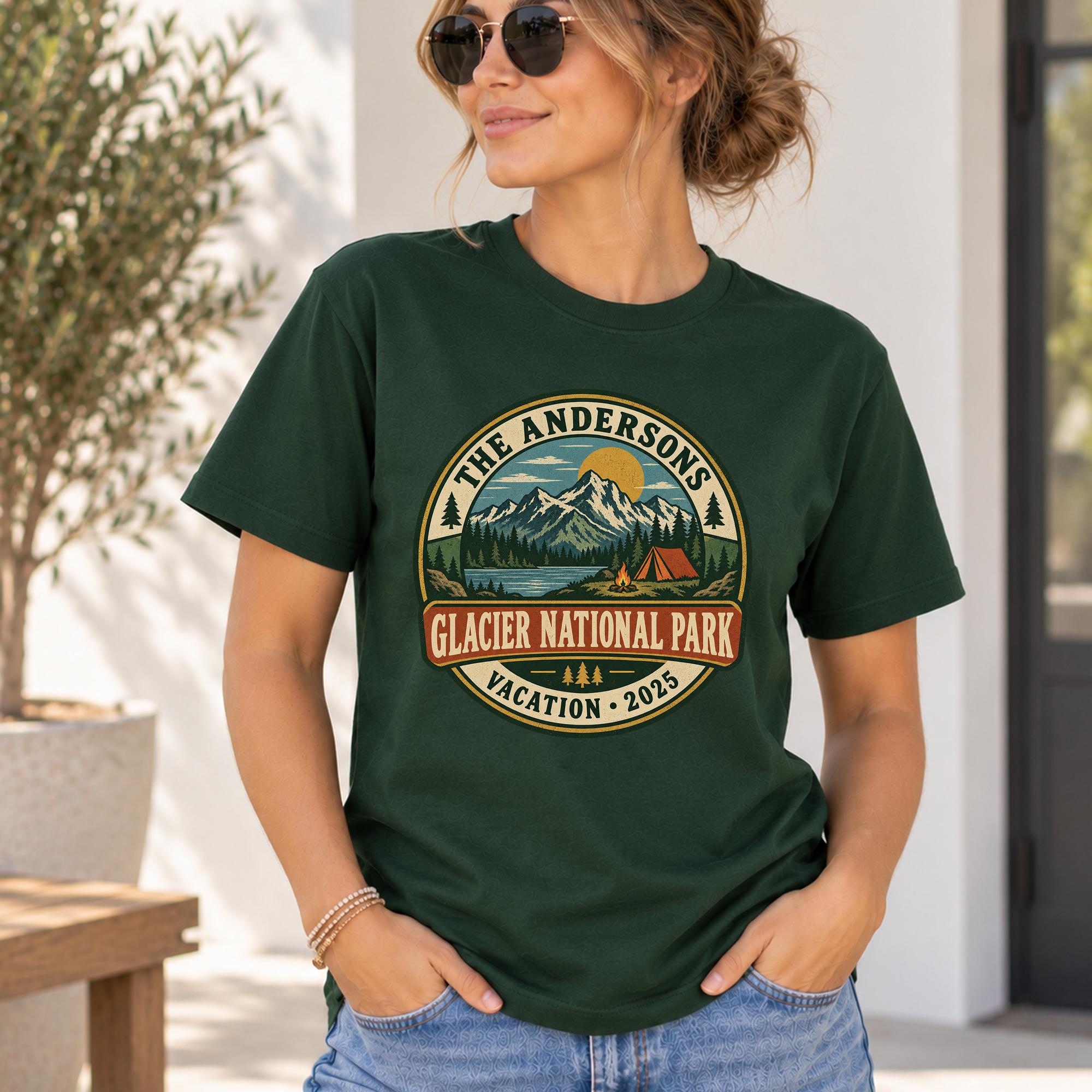 A woman wearing a green t-shirt with a graphic design of a mountain landscape and camping equipment, standing in front of a white wall with a potted plant.