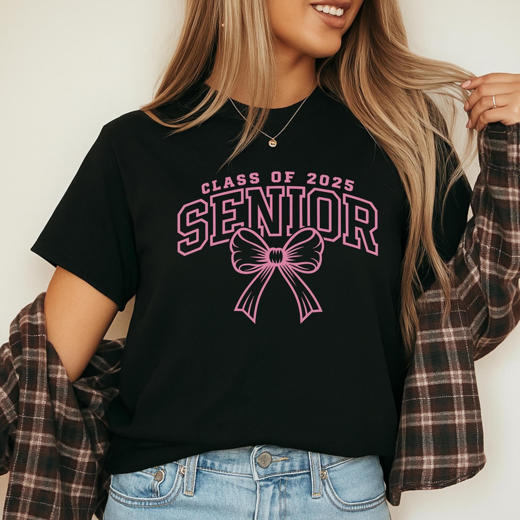 A woman wearing a black t-shirt with a pink bow and the text "CLASS OF 2025 SENIOR" printed on it.