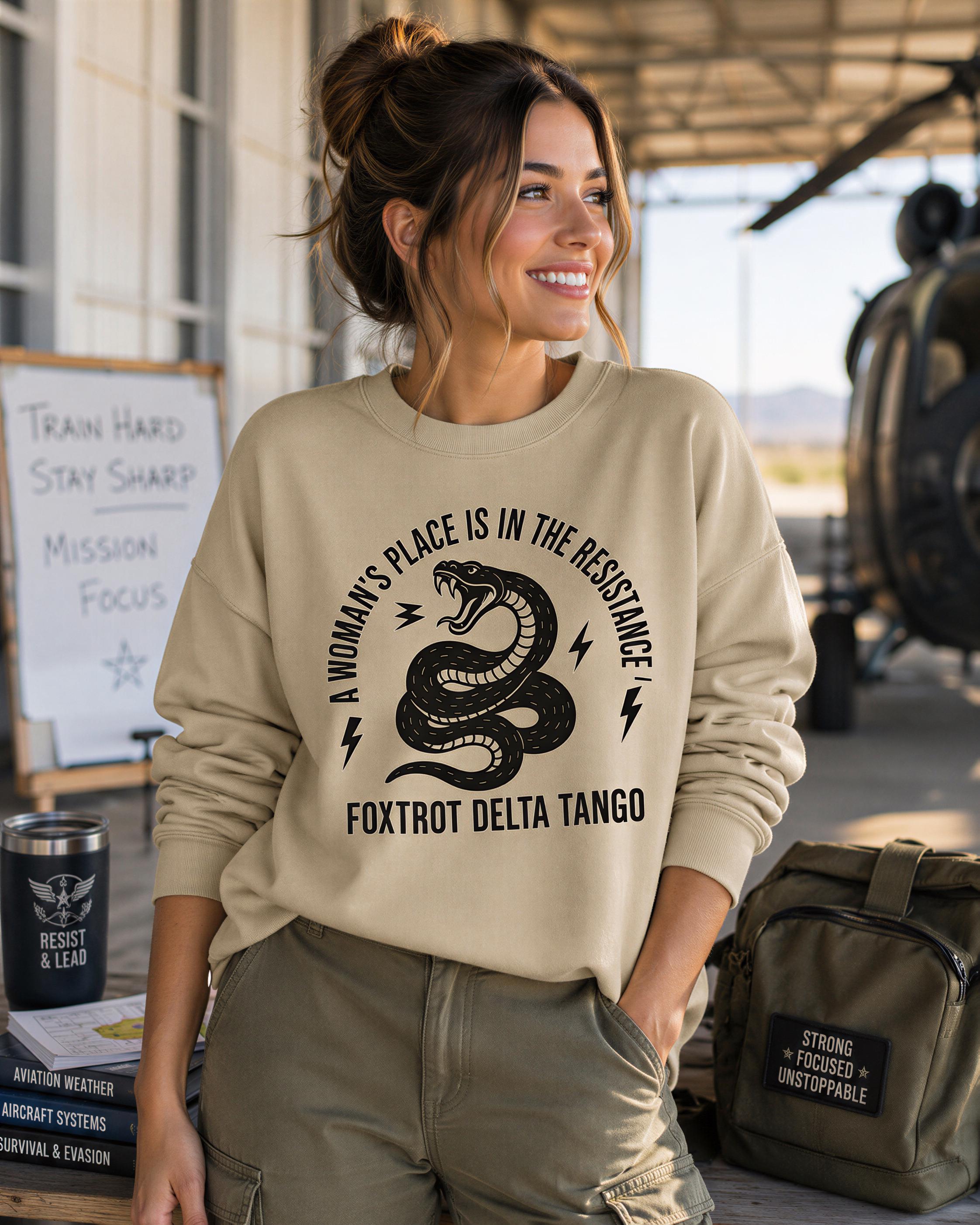 A woman wearing a beige sweatshirt with a graphic design stands in front of a sign that says "Train Hard Stay Sharp Mission Focus" and a book titled "Resist and Lead".