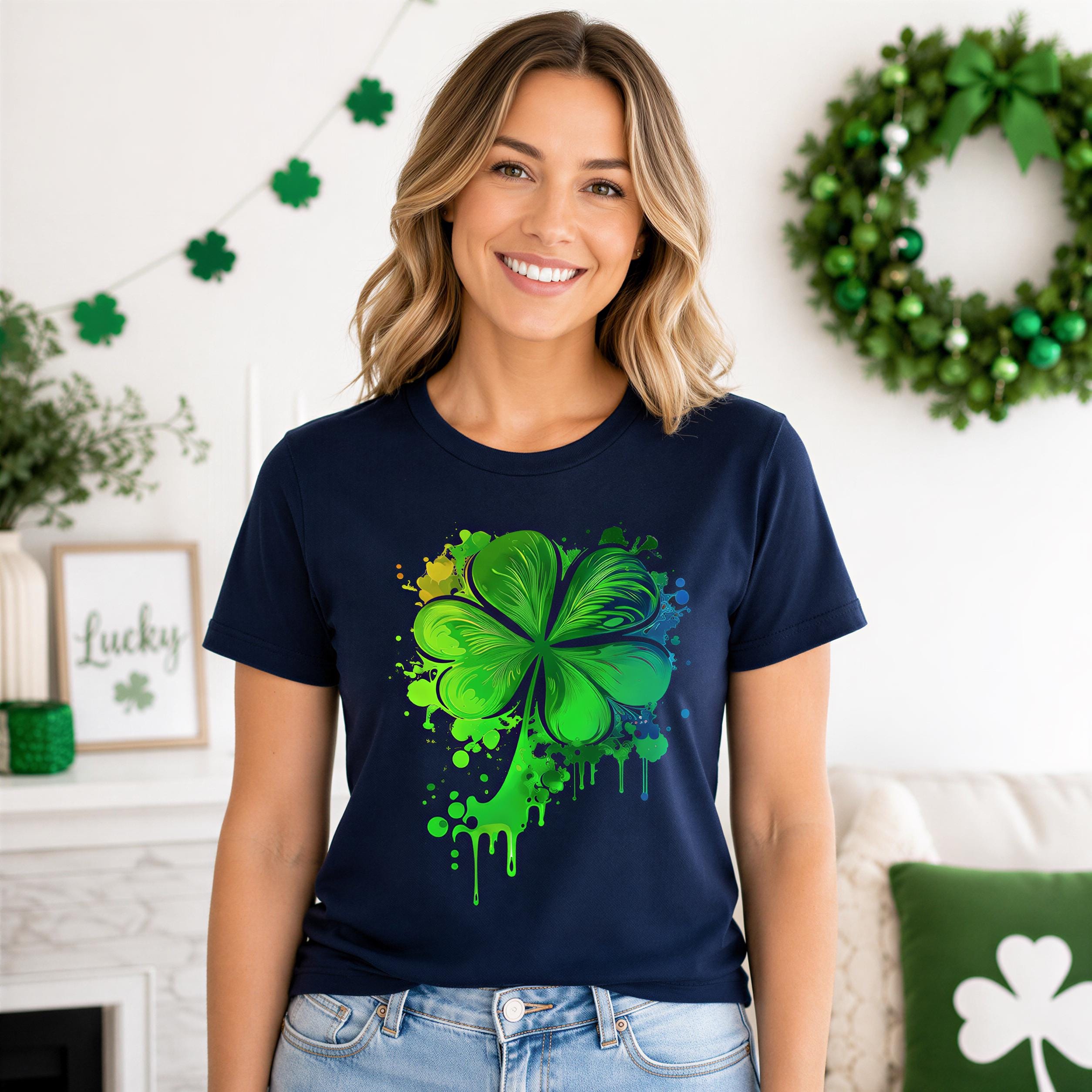 A woman wearing a navy blue t-shirt with a colorful green and yellow clover design stands in a room decorated for St. Patrick's Day.