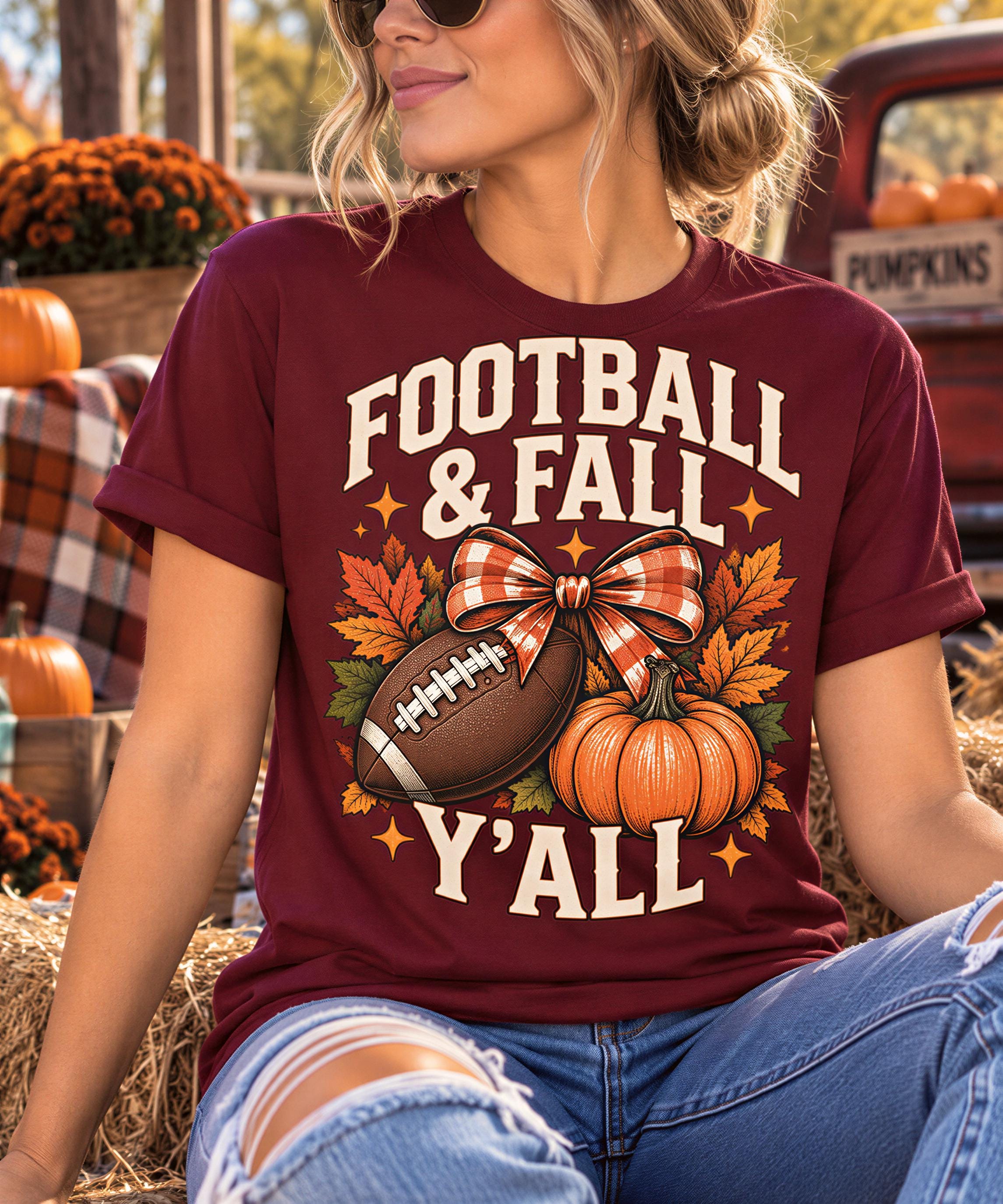 A woman wearing a maroon t-shirt with a graphic design of a football, pumpkins, and fall leaves, sitting on hay bales with a pumpkin decoration in the background.