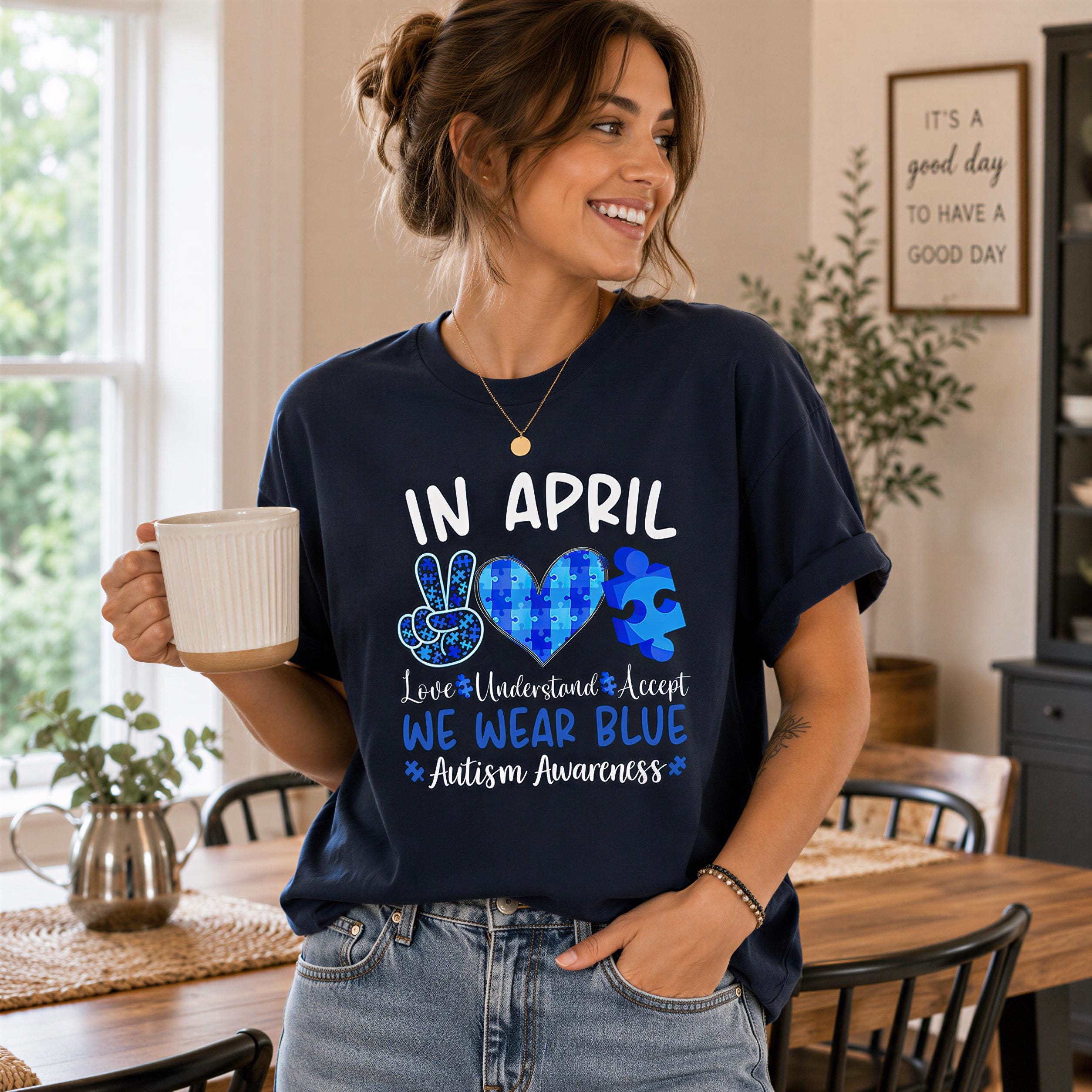 A woman wearing a navy blue t-shirt with a graphic design and text, smiling and holding a white mug.