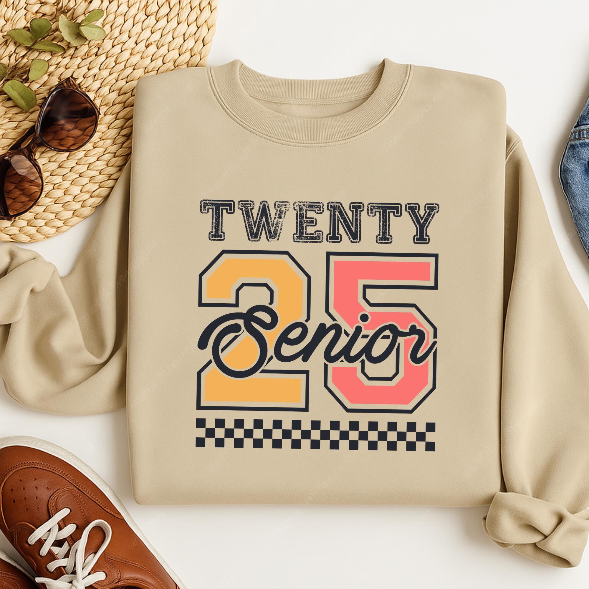 A beige sweatshirt with a graphic design that says "TWENTY 25 Senior" printed on it, along with a checkerboard pattern. The sweatshirt is placed on a white surface, and there are some sunglasses and a pair of shoes visible in the background.