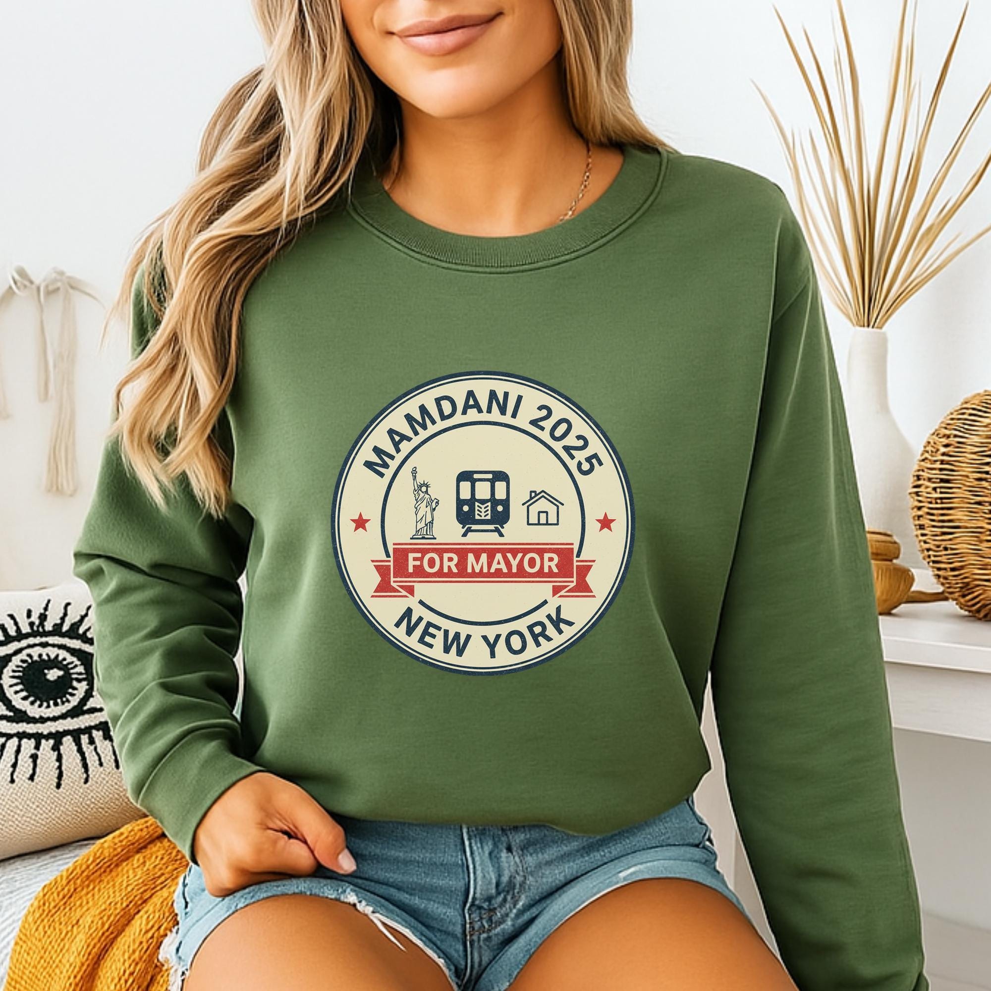 A woman wearing a green sweatshirt with a graphic design on it, sitting in a room with a vase and other decorative items.