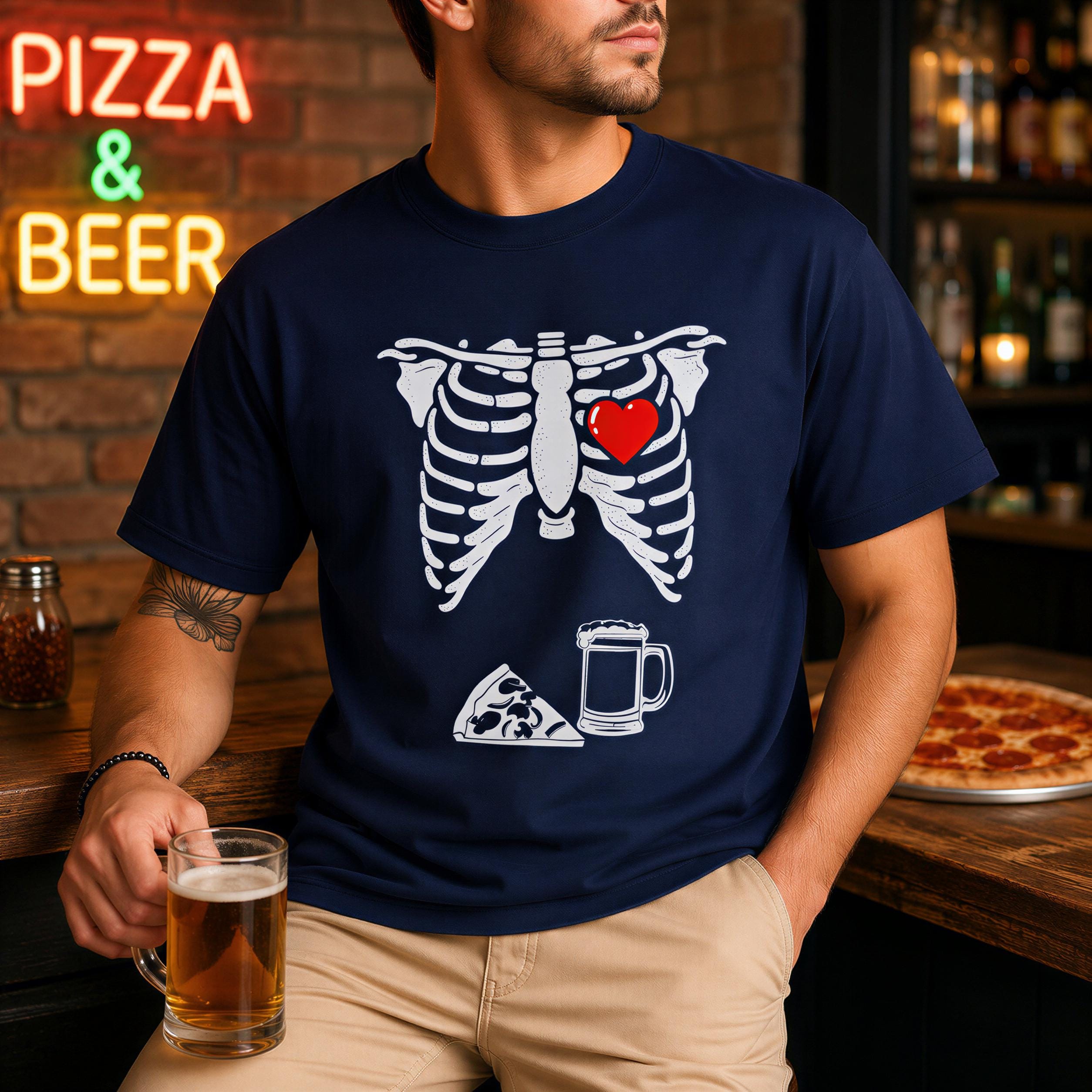 A man wearing a navy blue t-shirt with a graphic of a skeleton and a heart, holding a glass of beer in front of a brick wall with a neon sign that says 'PIZZA & BEER'.