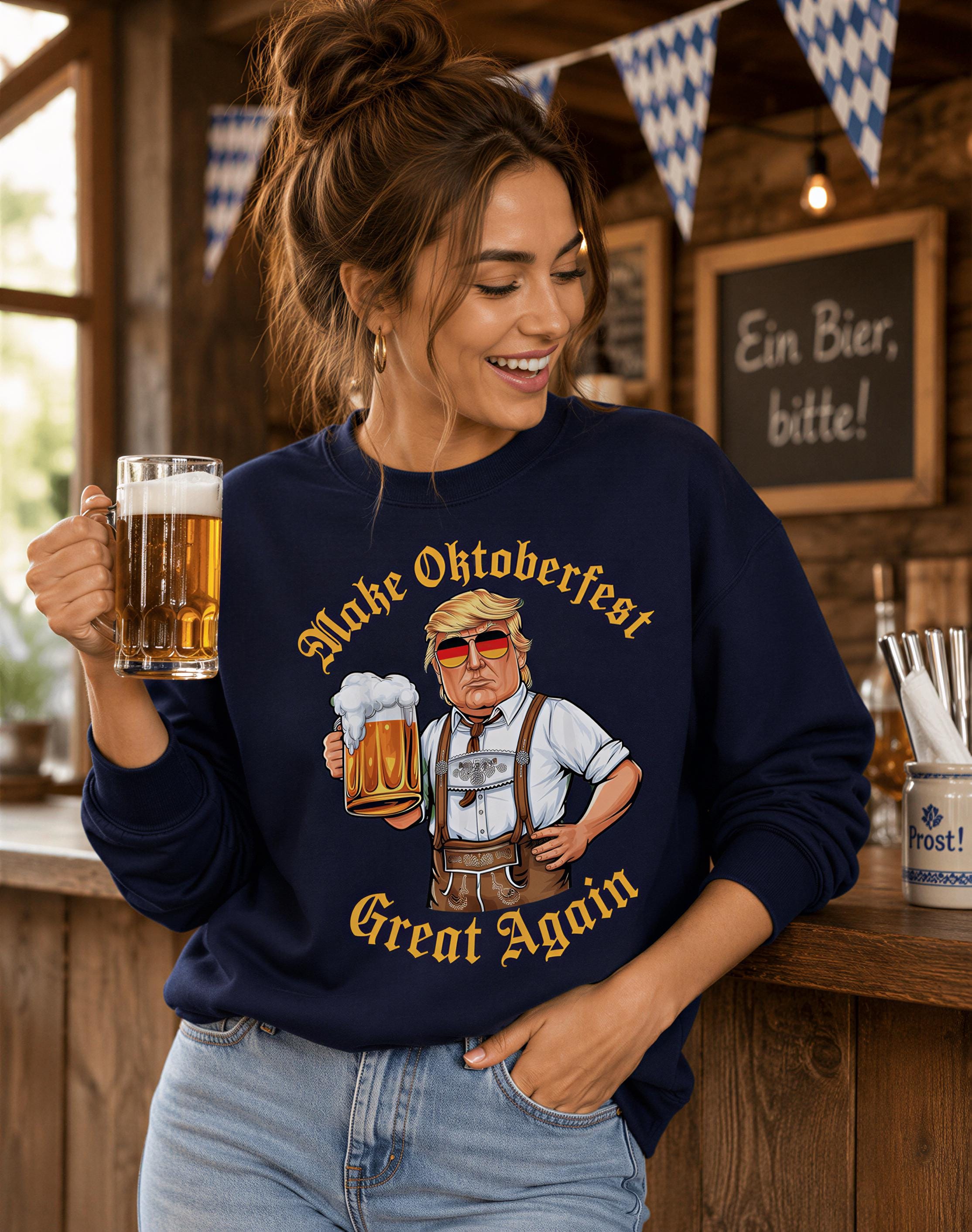 A woman wearing a navy blue sweatshirt with a cartoon image of a man holding a mug of beer and the text "Make Oktoberfest Great Again" is smiling and holding a glass of beer in a bar setting.