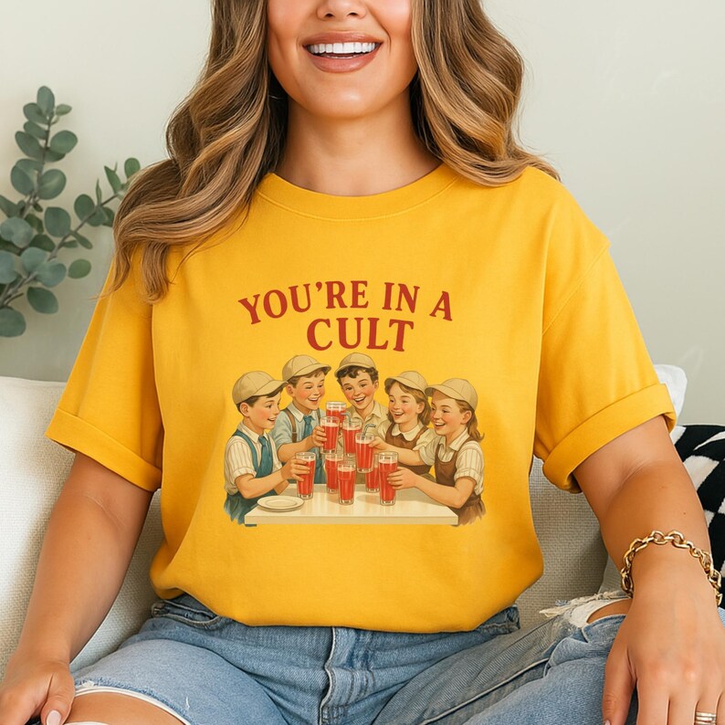 A woman wearing a yellow t-shirt with a graphic design of a group of people enjoying drinks at a table.