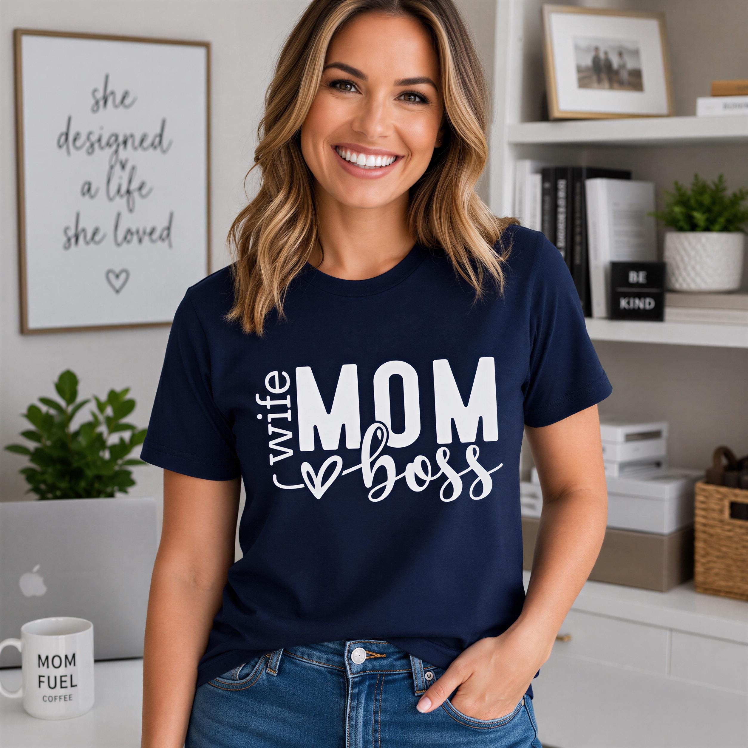 A smiling woman wearing a navy blue t-shirt with white text that says "she designed a life she loved" and "womom boss".