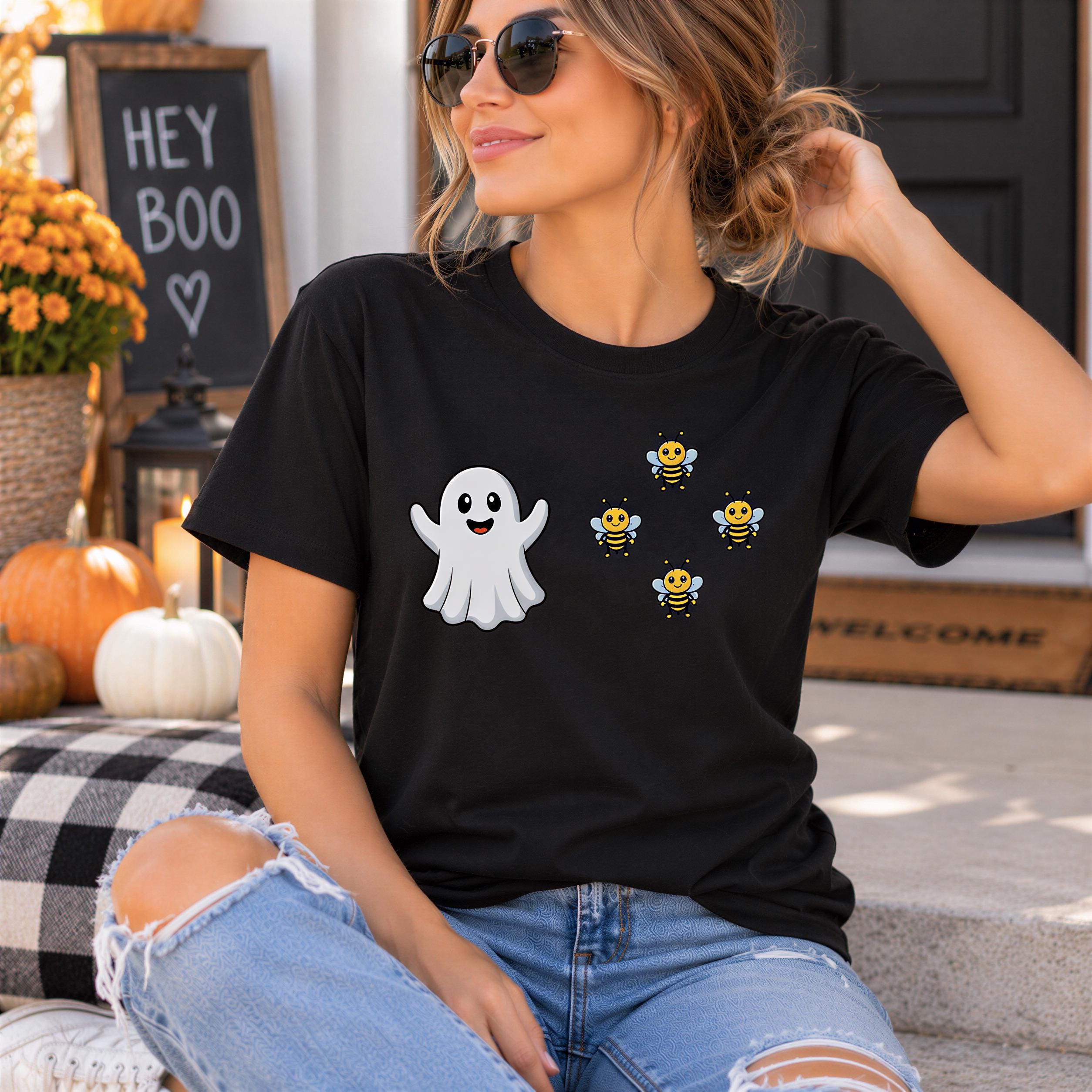 A woman wearing a black t-shirt with a ghost and four bees, sitting on a porch with Halloween decorations in the background.