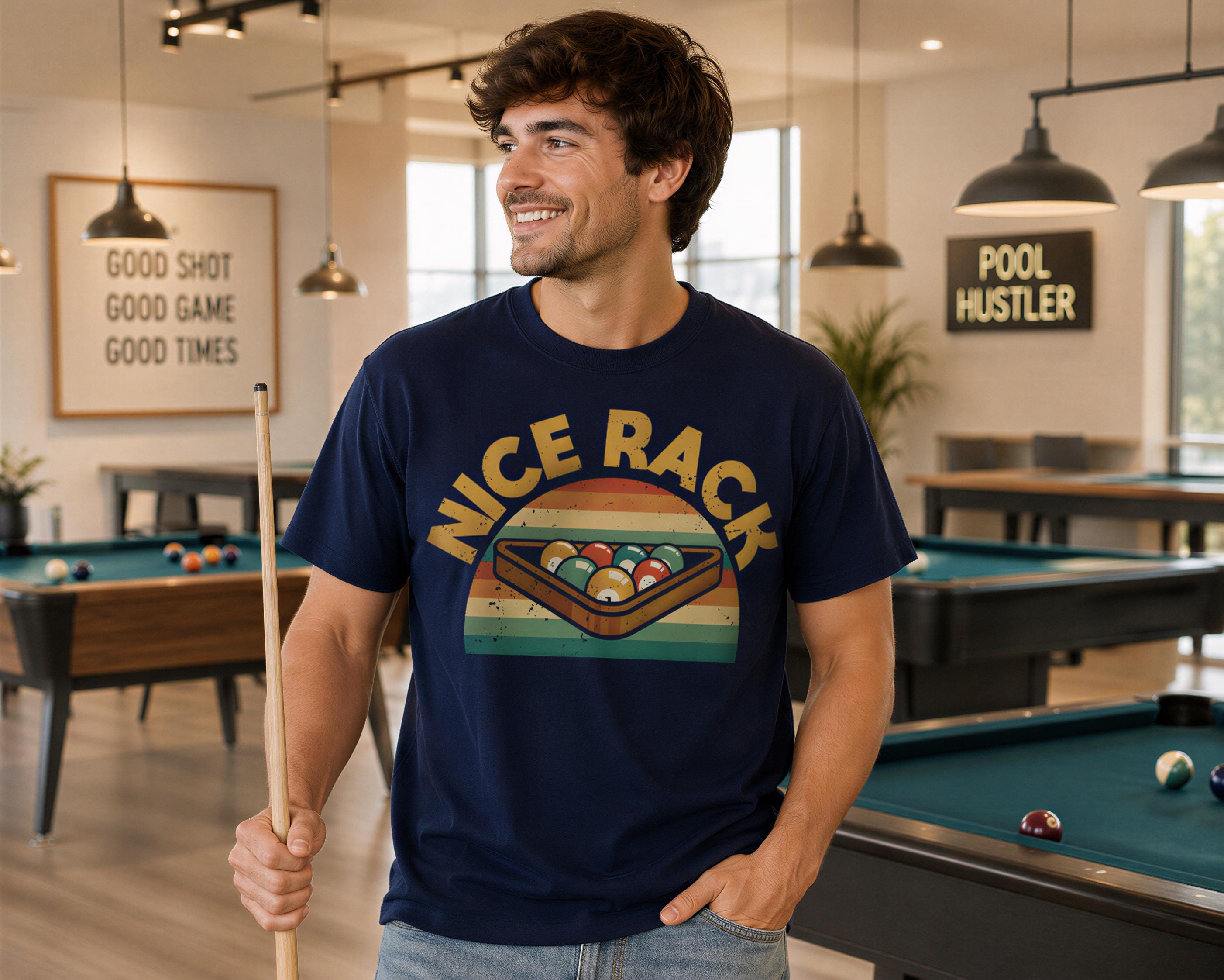 A man wearing a blue t-shirt with a graphic of a pool rack and the text "nice rack" is standing in a room with pool tables and a "pool hustler" sign.