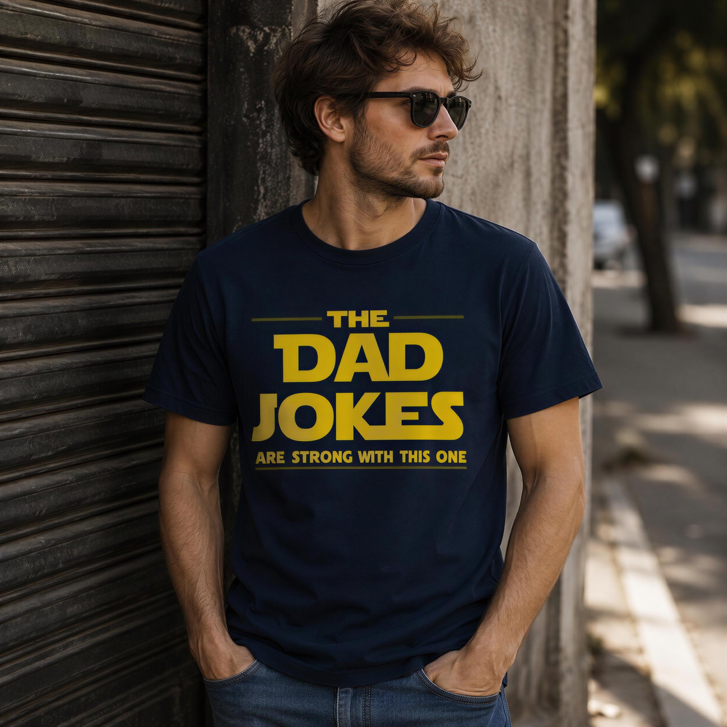 A man wearing a navy blue t-shirt with the text "THE DAD JOKES ARE STRONG WITH THIS ONE" printed on it, standing in front of a metal shutter.