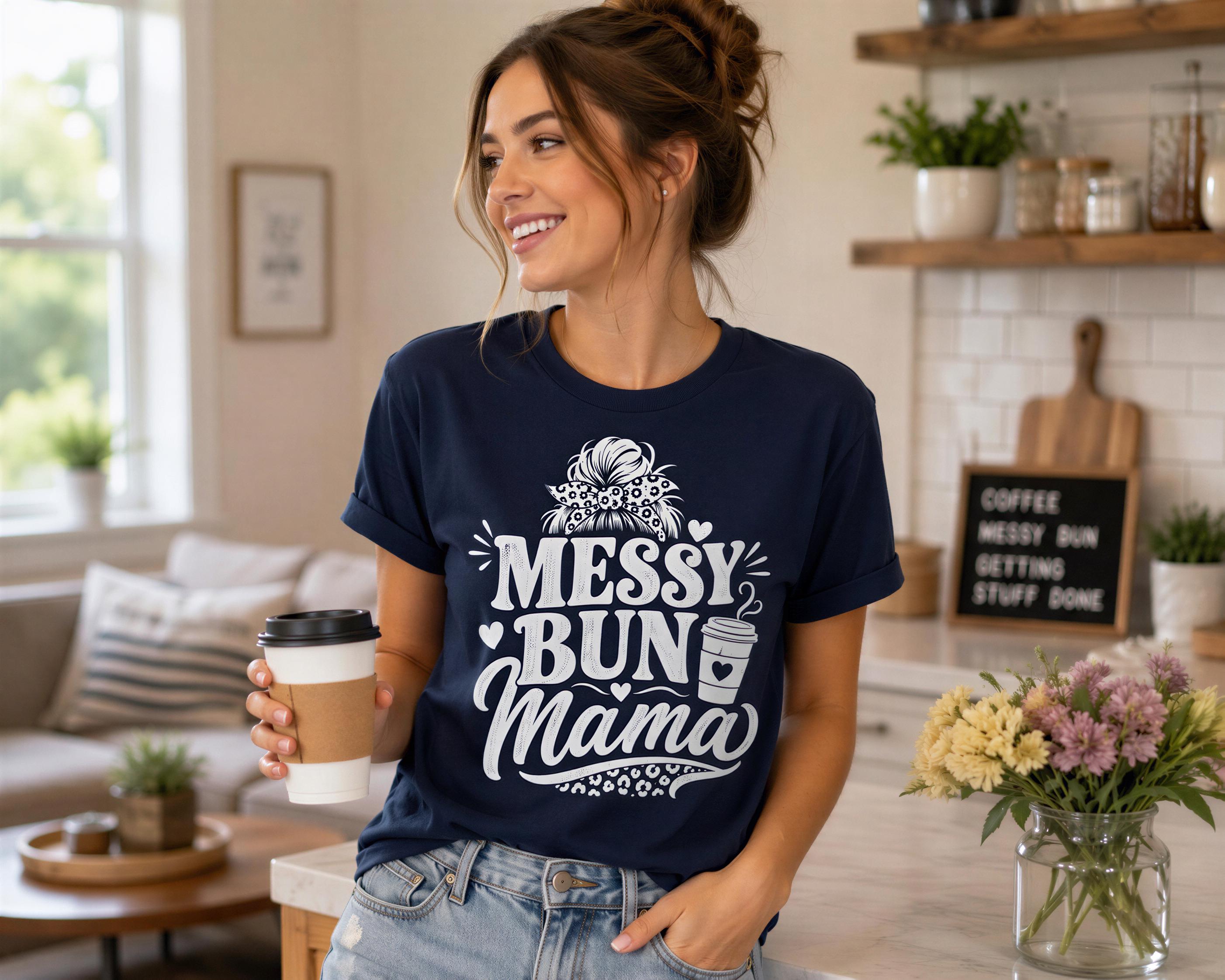 A woman wearing a navy blue t-shirt with the text "MESSY BUN MAMA" is holding a coffee cup and smiling in a cozy kitchen setting.