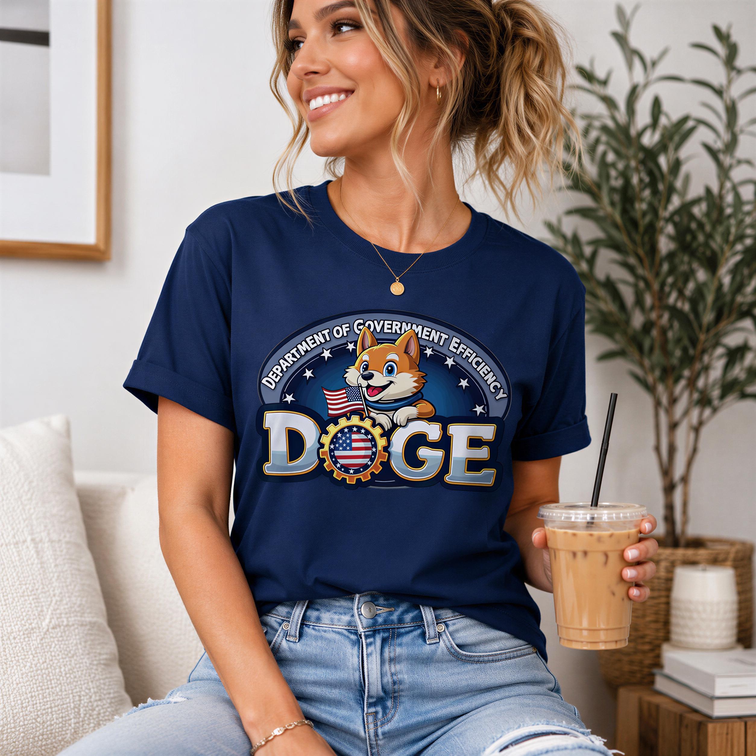 A woman wearing a navy blue t-shirt with a cartoon dog and the text "DEPARTMENT OF GOVERNMENT EFFICIENCY DOGE" is sitting on a couch and holding a drink.