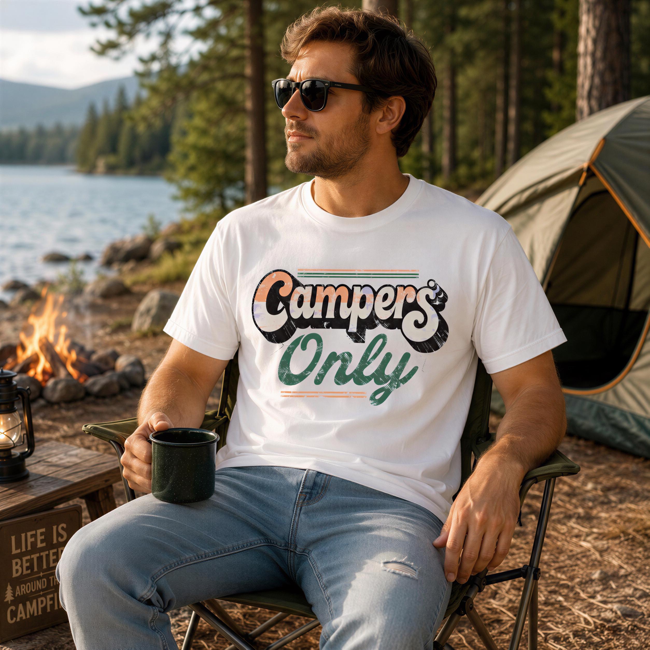 A man wearing a white t-shirt with a graphic design sits in a chair near a campfire, holding a mug and looking off to the side.