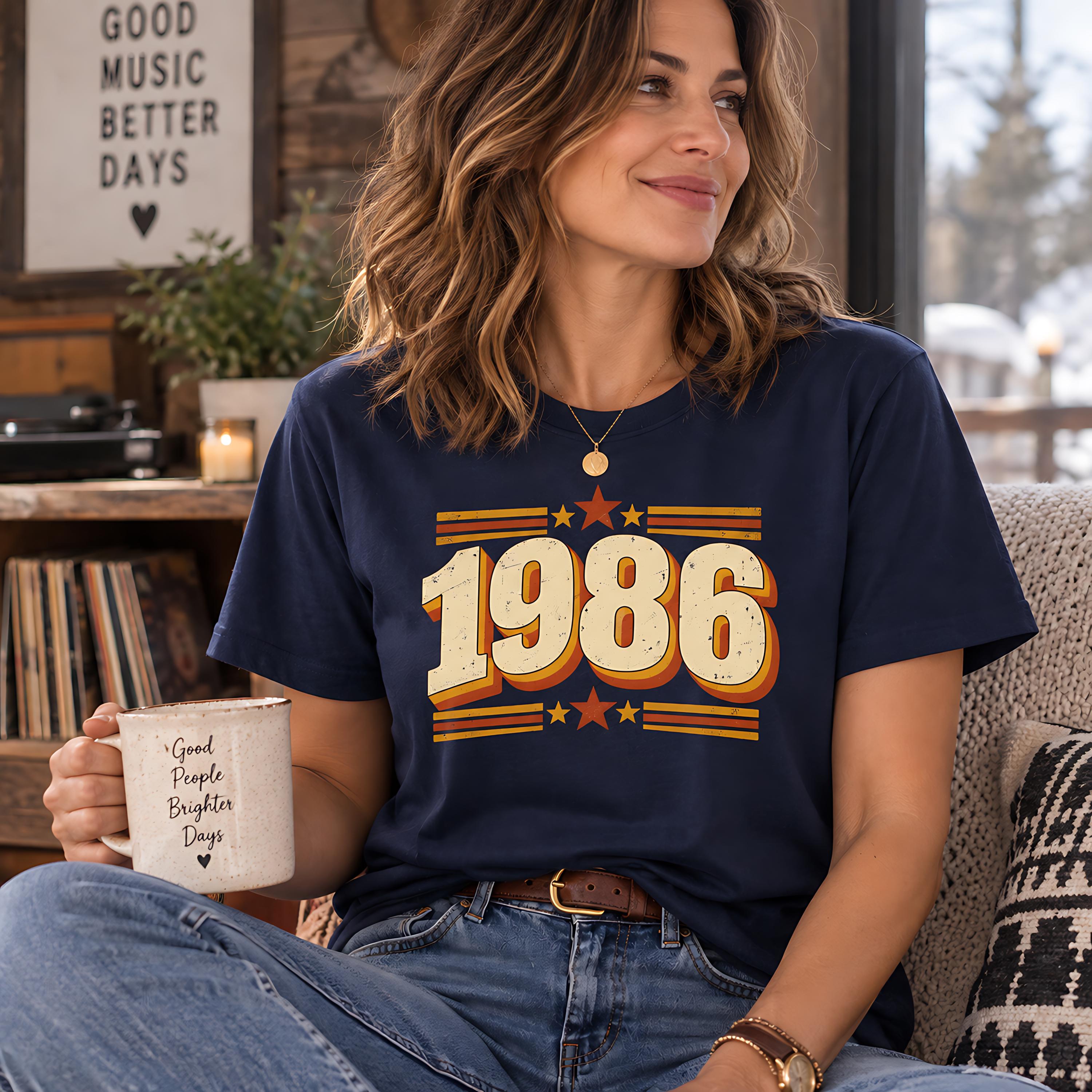 A woman wearing a navy blue t-shirt with the number 1986 and a mug with the text "Good People Enjoy Better Days" is sitting on a couch, smiling and holding a mug.