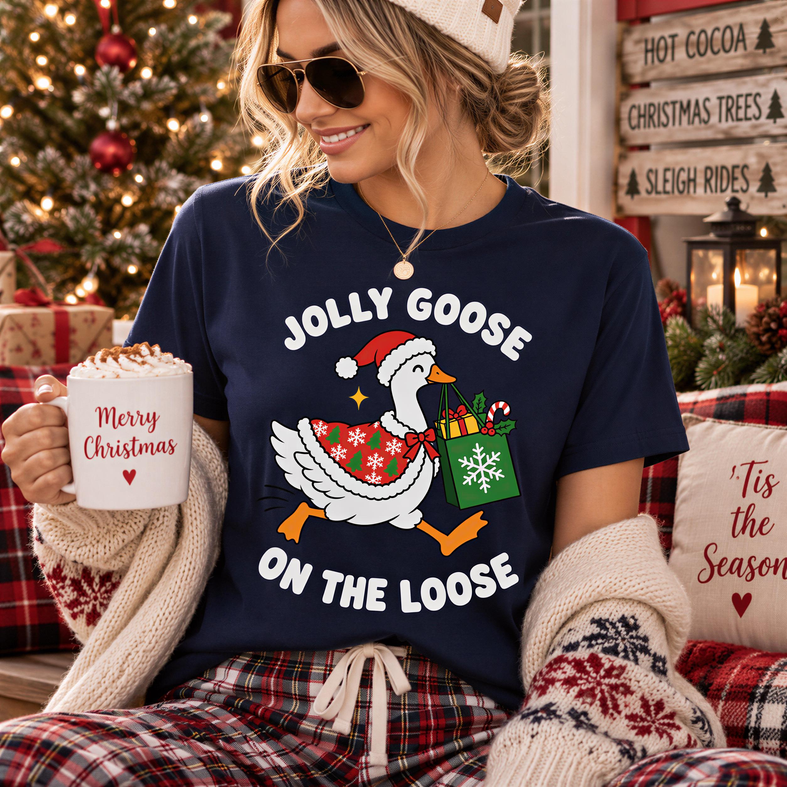 A woman wearing a navy blue t-shirt with a cartoon goose holding a gift bag and a mug with "Merry Christmas" written on it, smiling and holding a pillow with "Tis the Season" written on it.