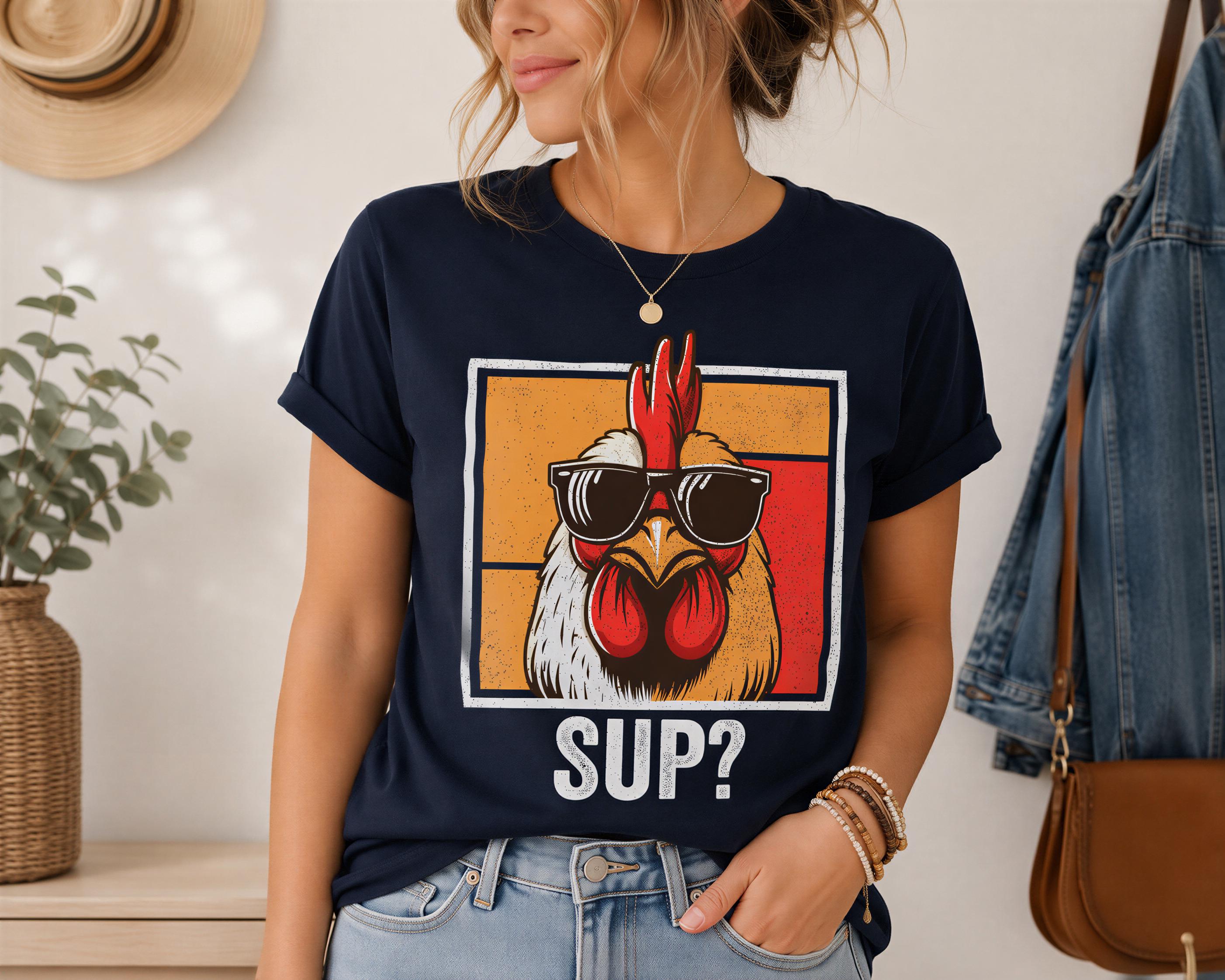 A woman wearing a navy blue t-shirt with a graphic of a rooster wearing sunglasses and the text "SUP?"