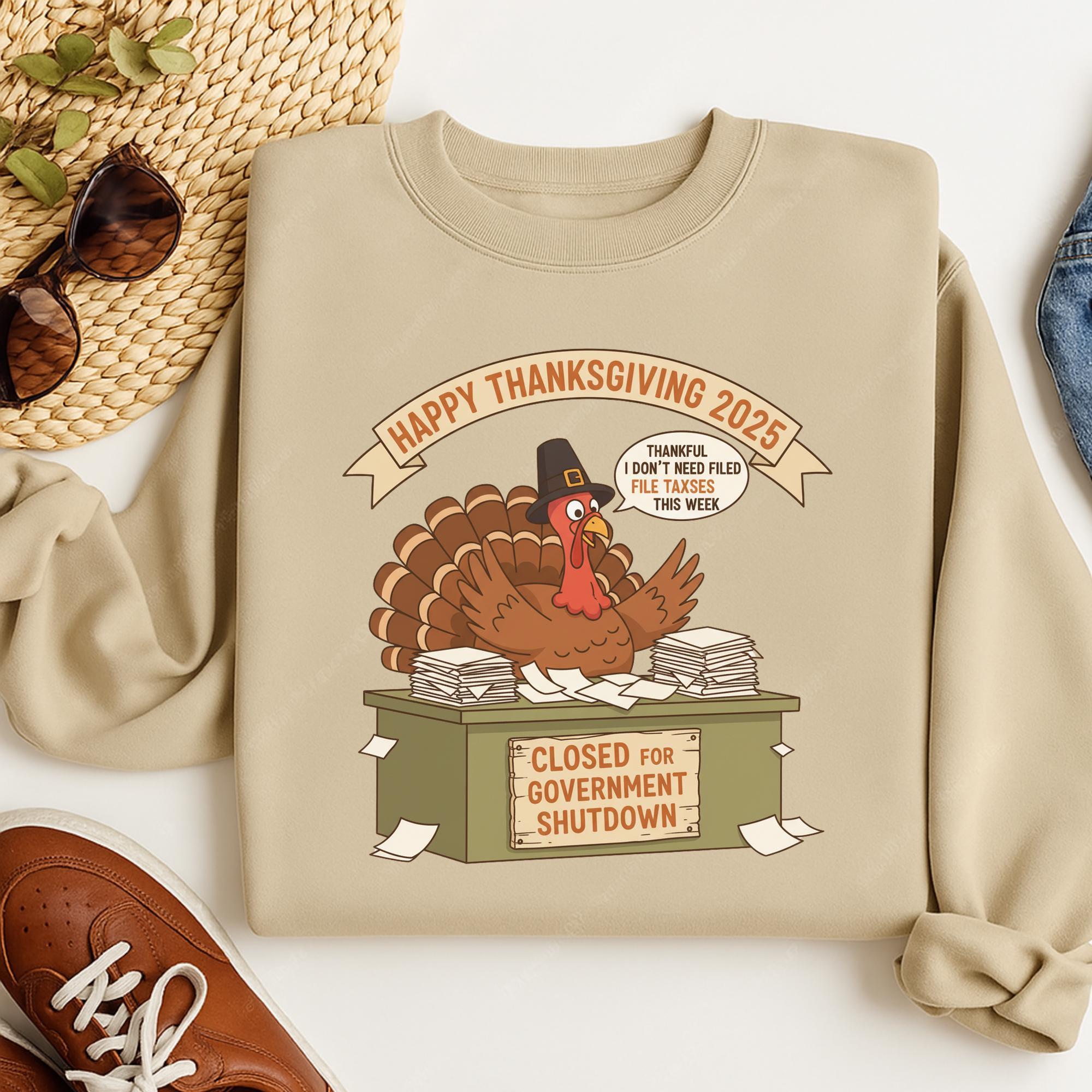 A beige sweatshirt with a graphic of a turkey sitting on a desk with a sign that says "CLOSED FOR GOVERNMENT SHUTDOWN".
