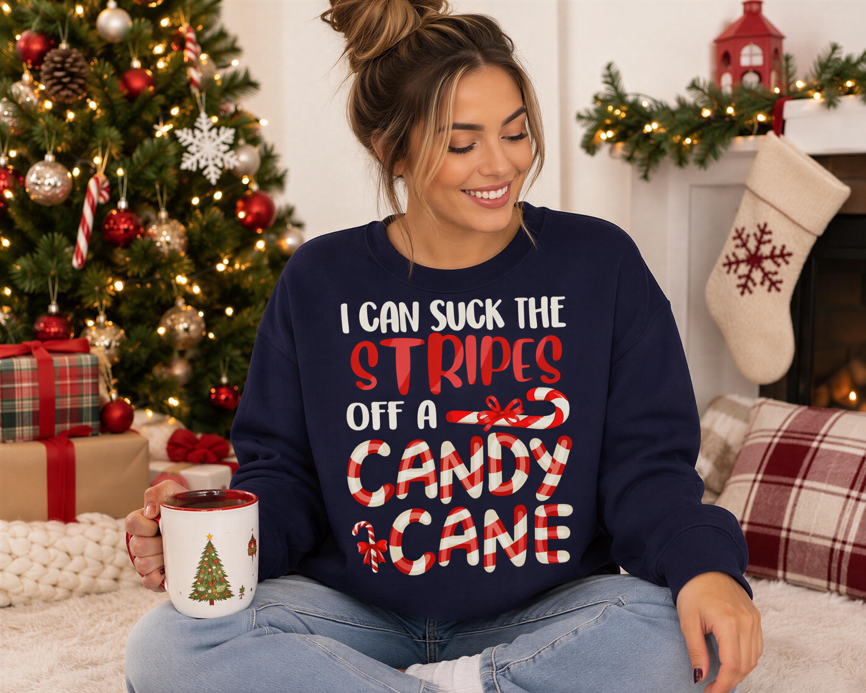 A woman sitting on the floor in front of a Christmas tree, holding a mug and wearing a blue sweatshirt with a humorous text.