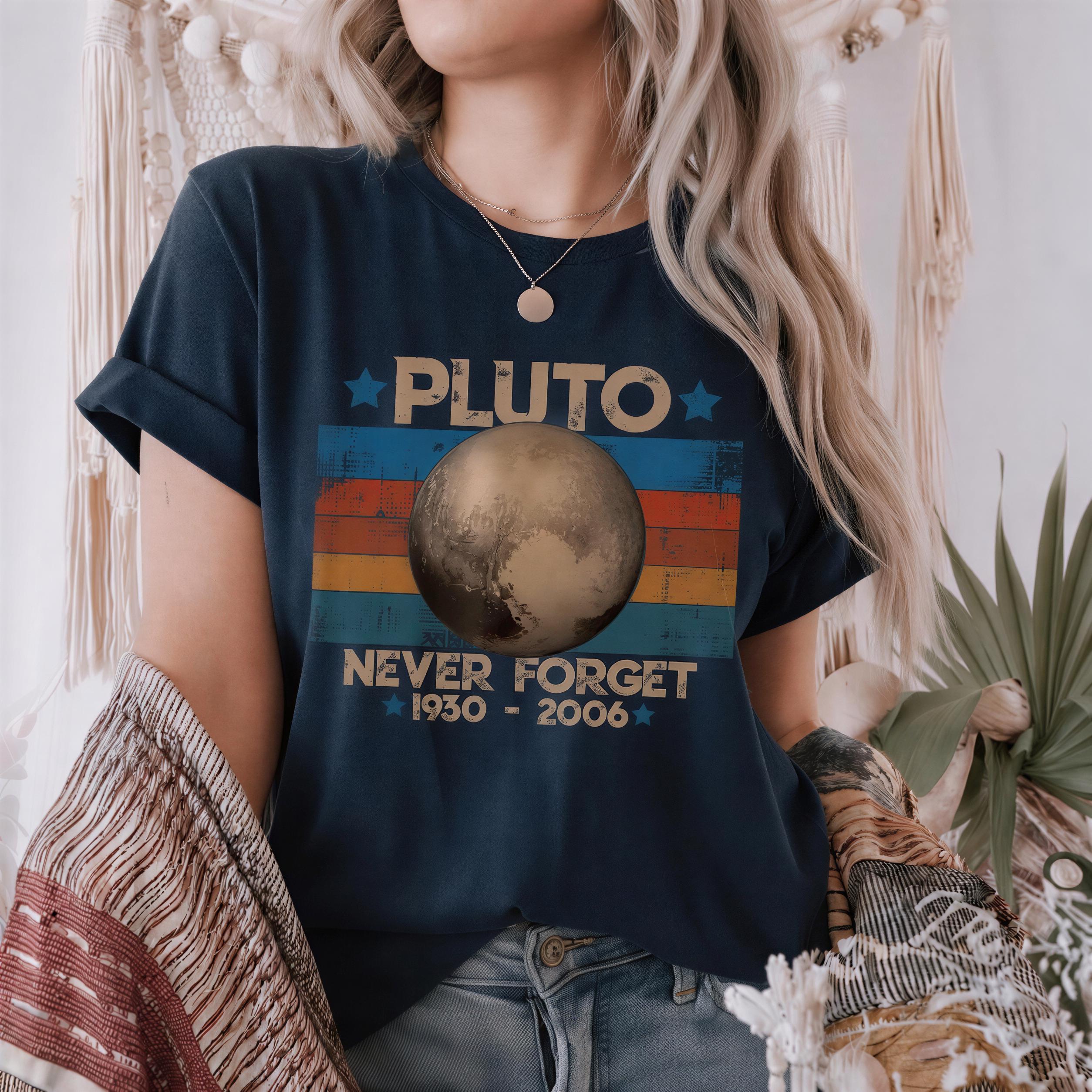 A woman wearing a blue t-shirt with a graphic design featuring a planet and the text "PLUTO NEVER FORGET 1930-2006".