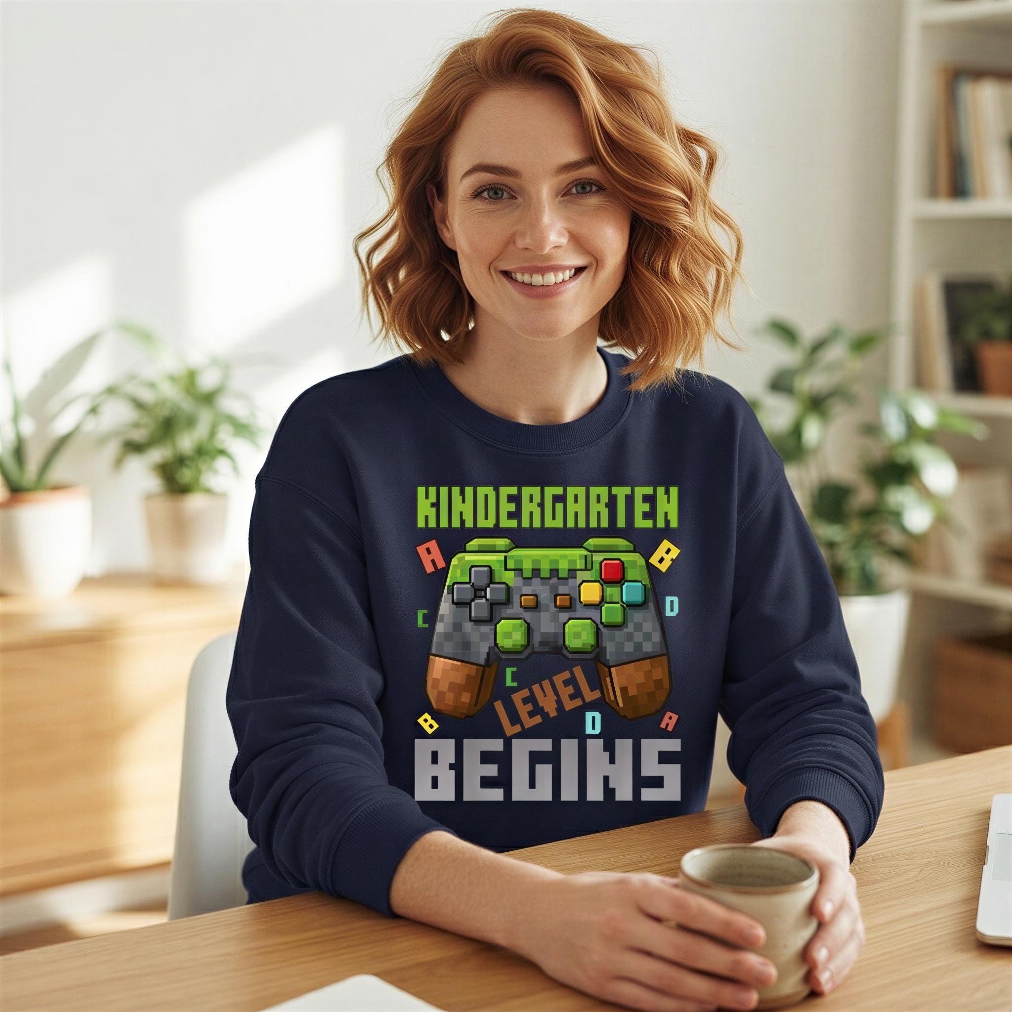 A woman wearing a blue sweatshirt with a graphic design on it, sitting at a desk and smiling.