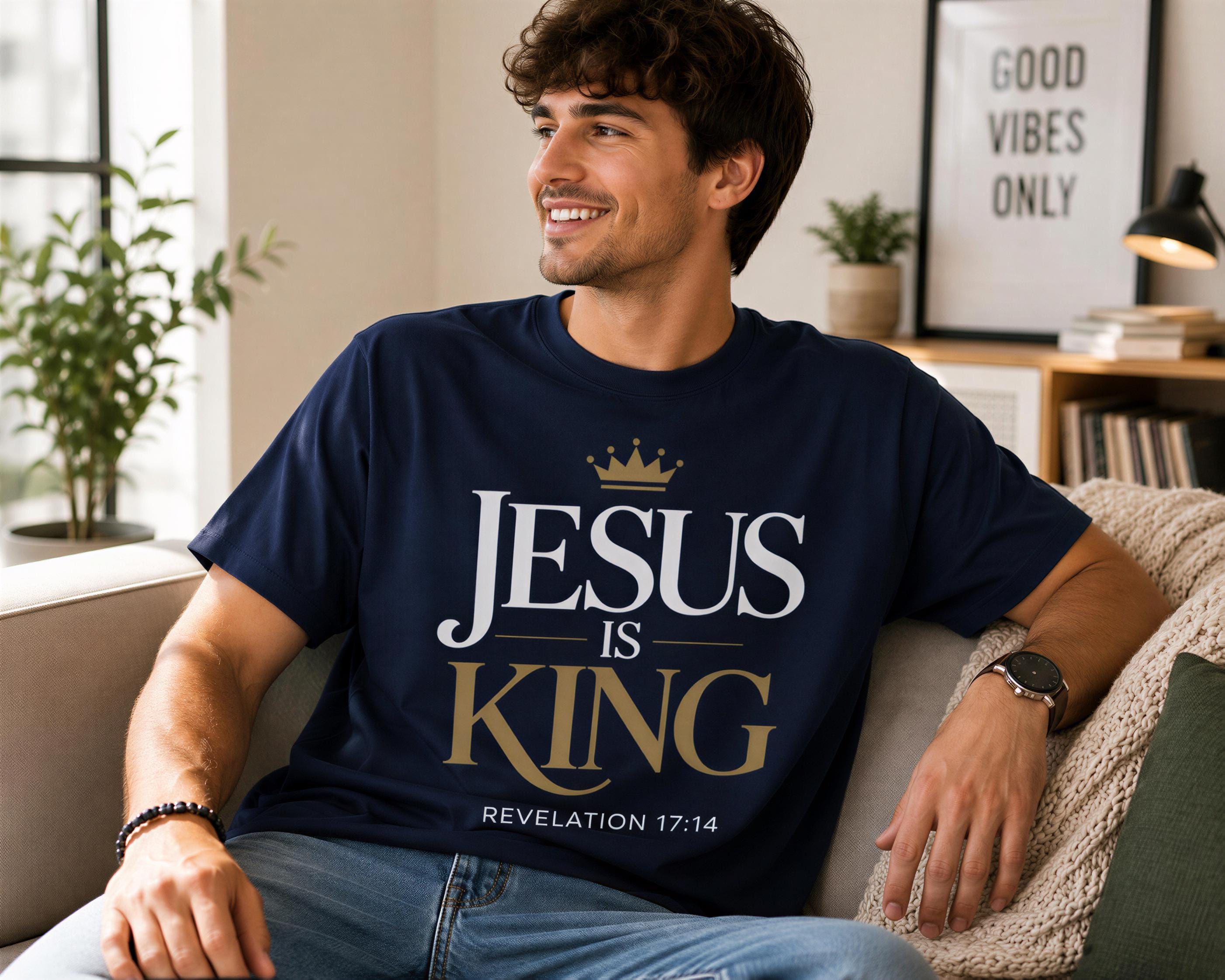A man wearing a blue t-shirt with the text "JESUS IS KING" and "REVELATION 17:14" is sitting on a couch in a living room.