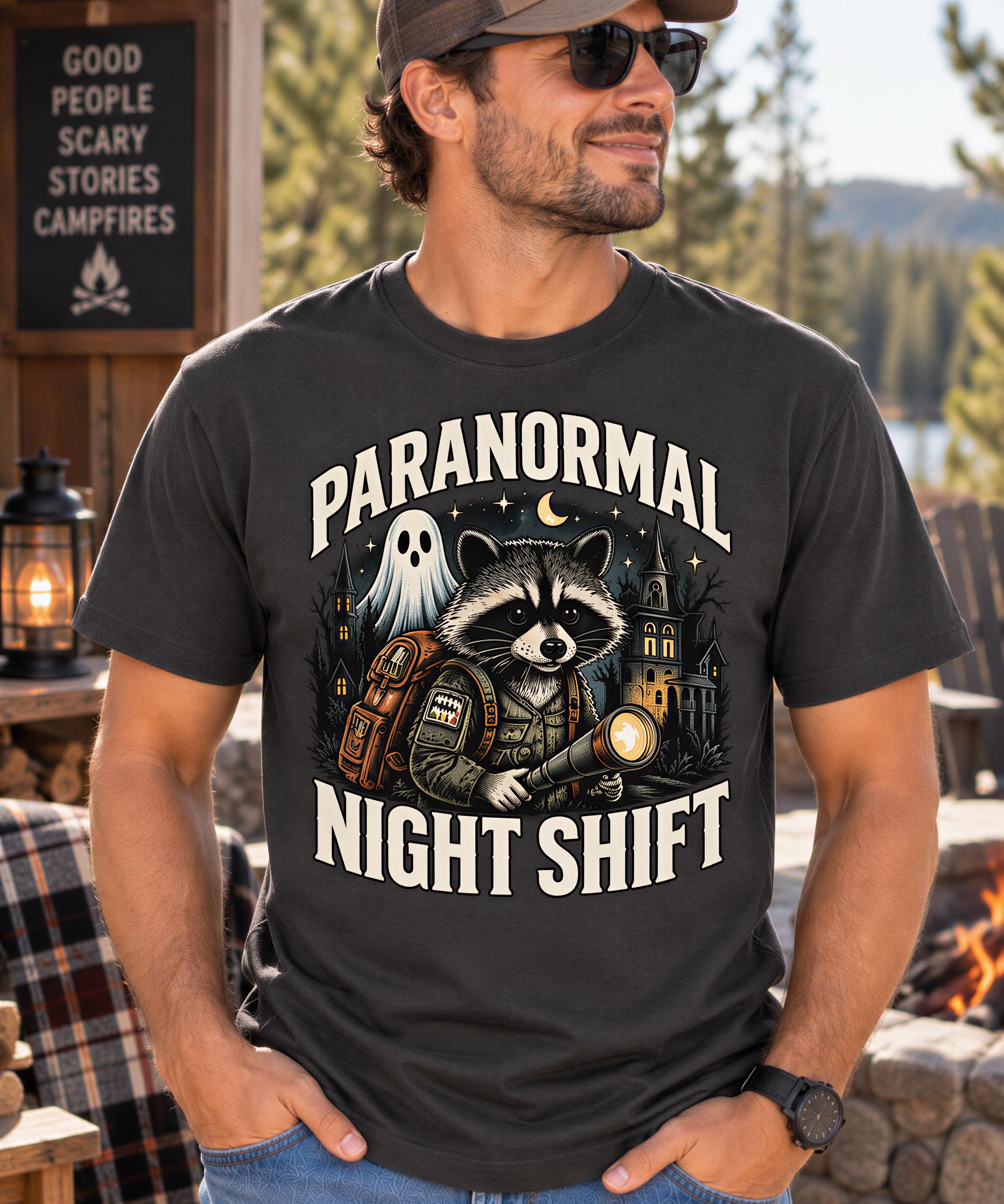 A man wearing a t-shirt with a graphic design of a raccoon holding a flashlight and a ghost, along with the text "PARANORMAL NIGHT SHIFT".