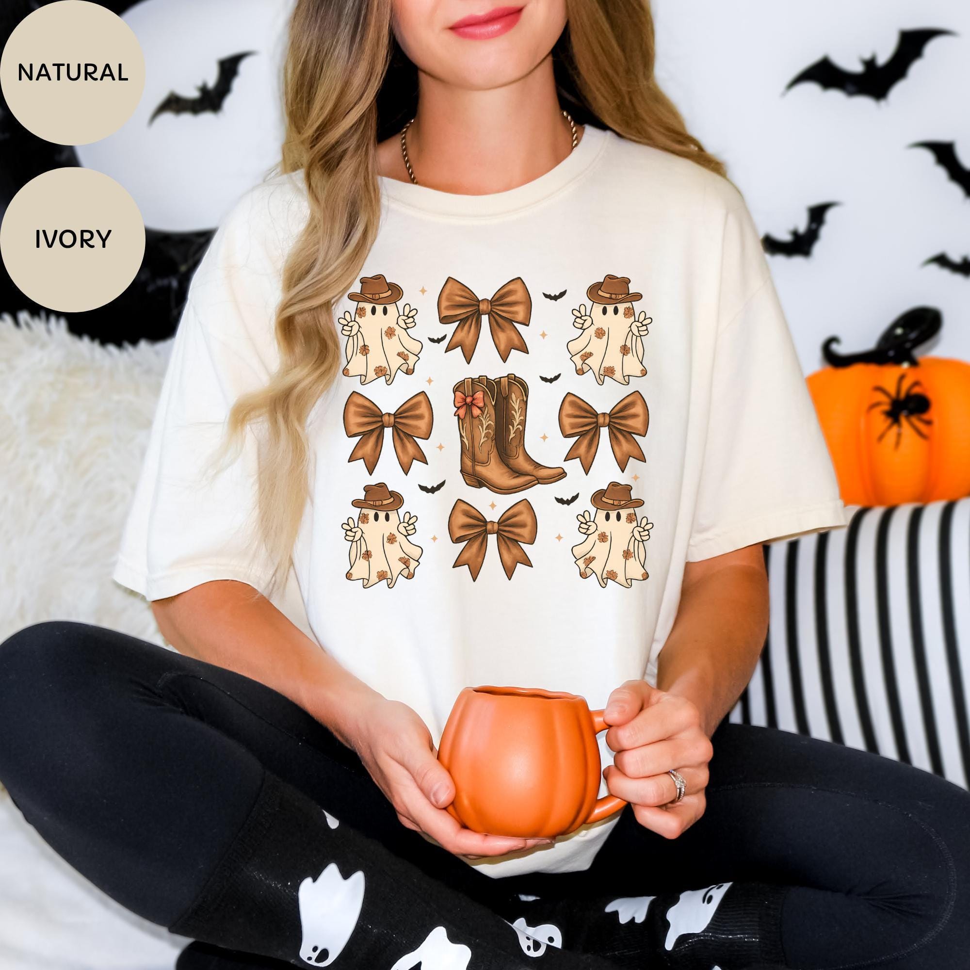 A woman wearing a white t-shirt with a graphic design of ghostly figures and brown bows, holding a pumpkin-shaped mug.