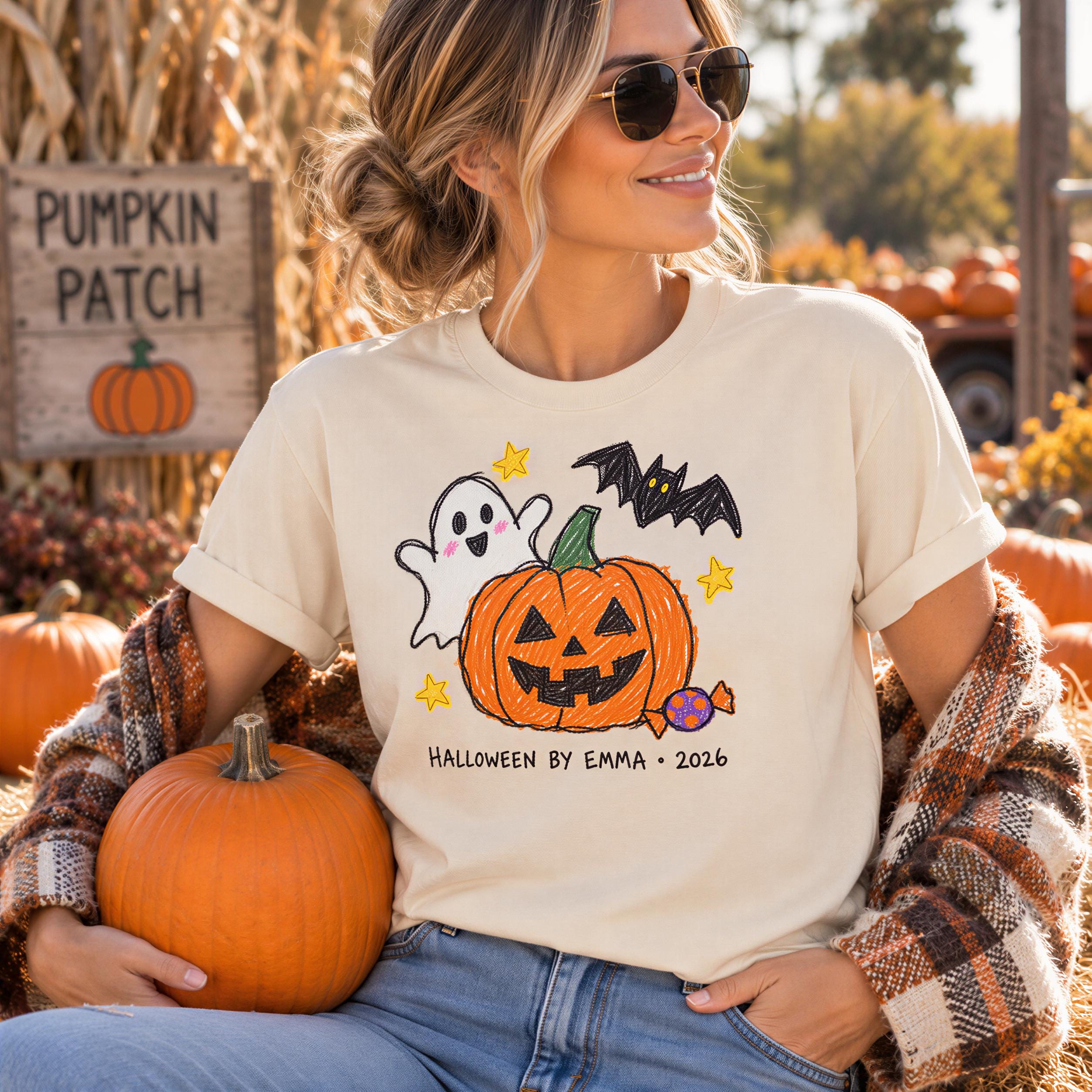 A woman wearing a Halloween-themed t-shirt and sunglasses is sitting in front of a pumpkin patch, holding a pumpkin.