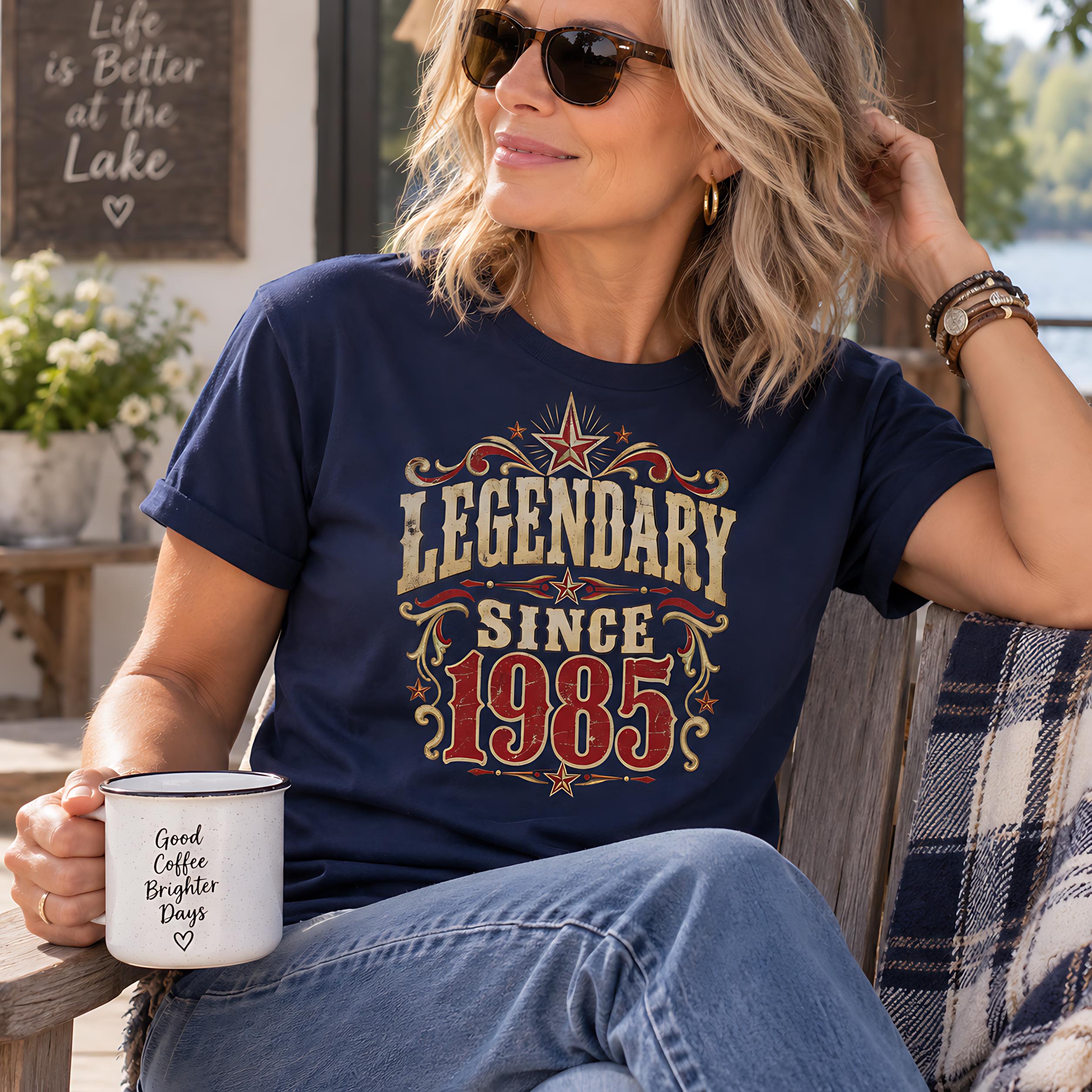 A woman wearing sunglasses and a navy blue t-shirt with a graphic design is sitting on a bench, holding a white mug with text on it.