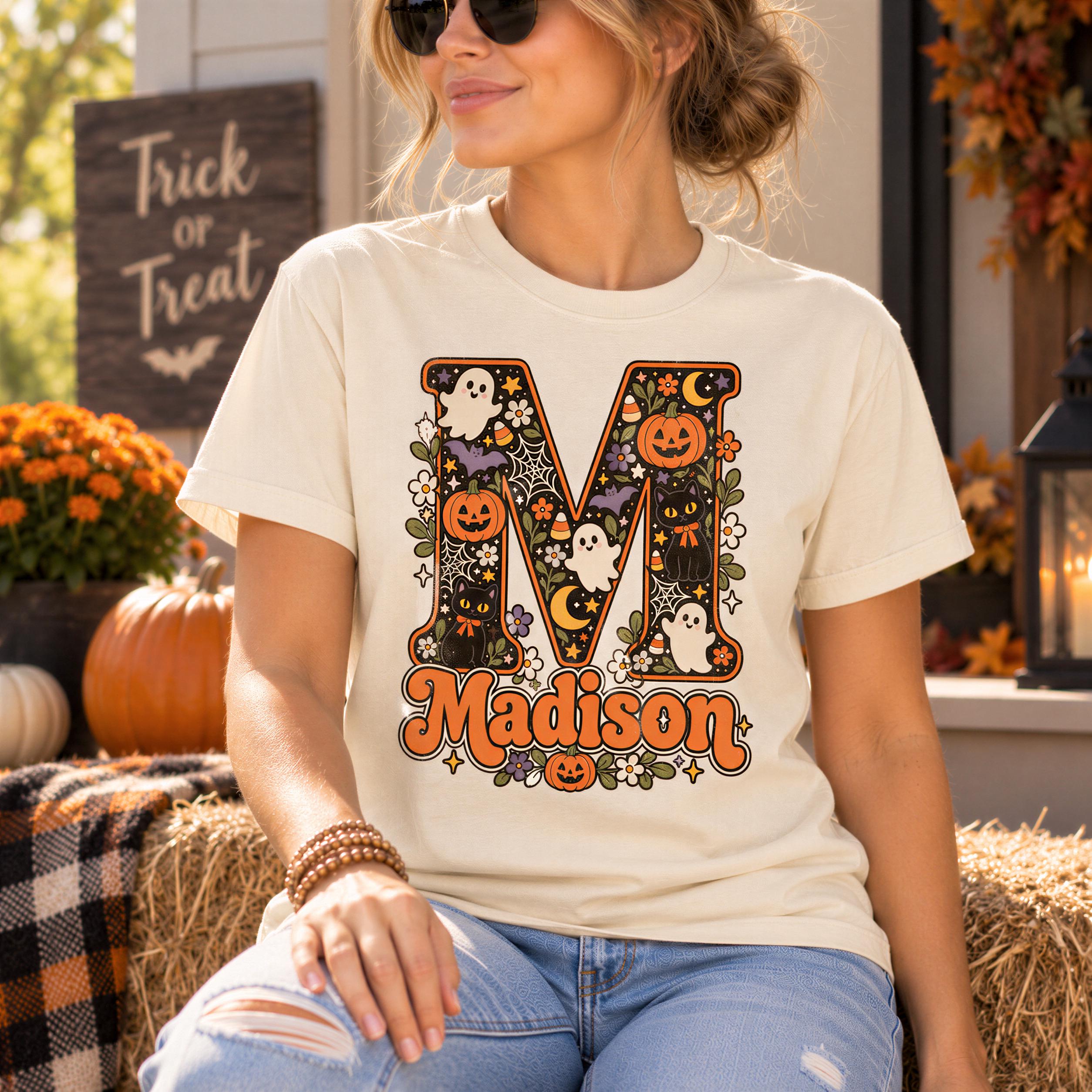 A woman wearing a white t-shirt with a Halloween-themed graphic and the name "Madison" printed on it, sitting on a hay bale.