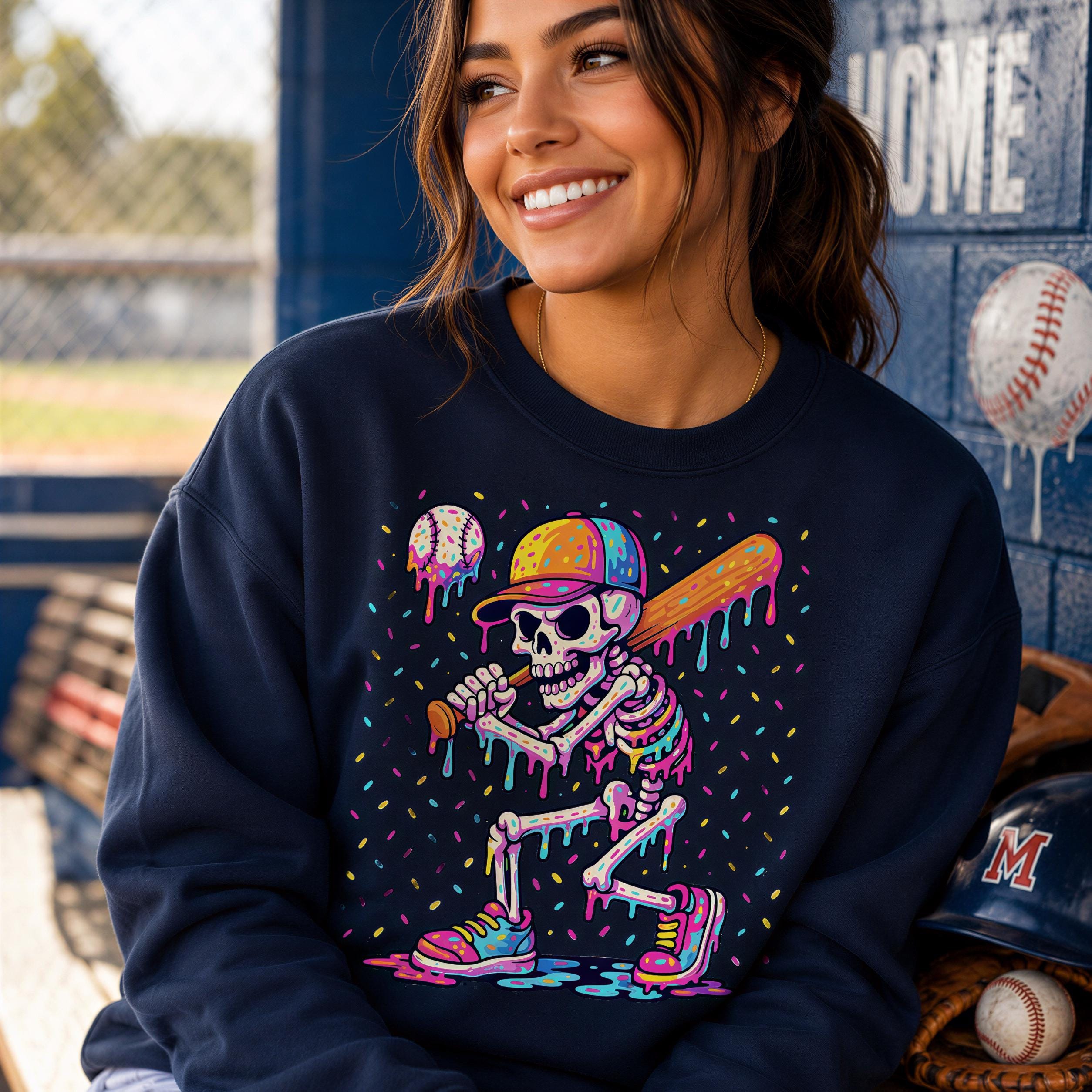 A smiling woman wearing a navy blue sweatshirt with a colorful graphic of a skeleton playing baseball.