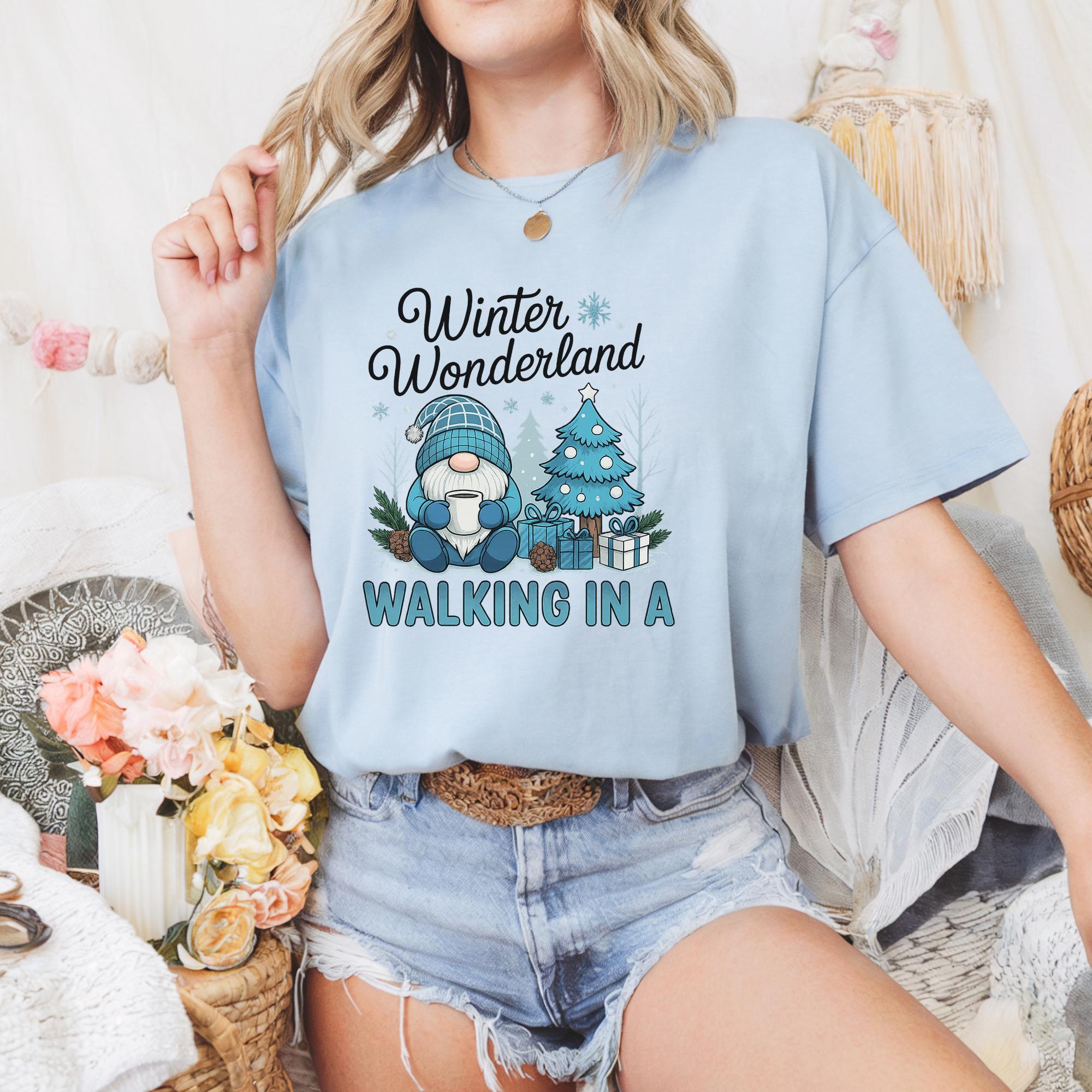A woman wearing a light blue t-shirt with a graphic design of a gnome and a Christmas tree, along with the text "Winter Wonderland" and "Walking in a".