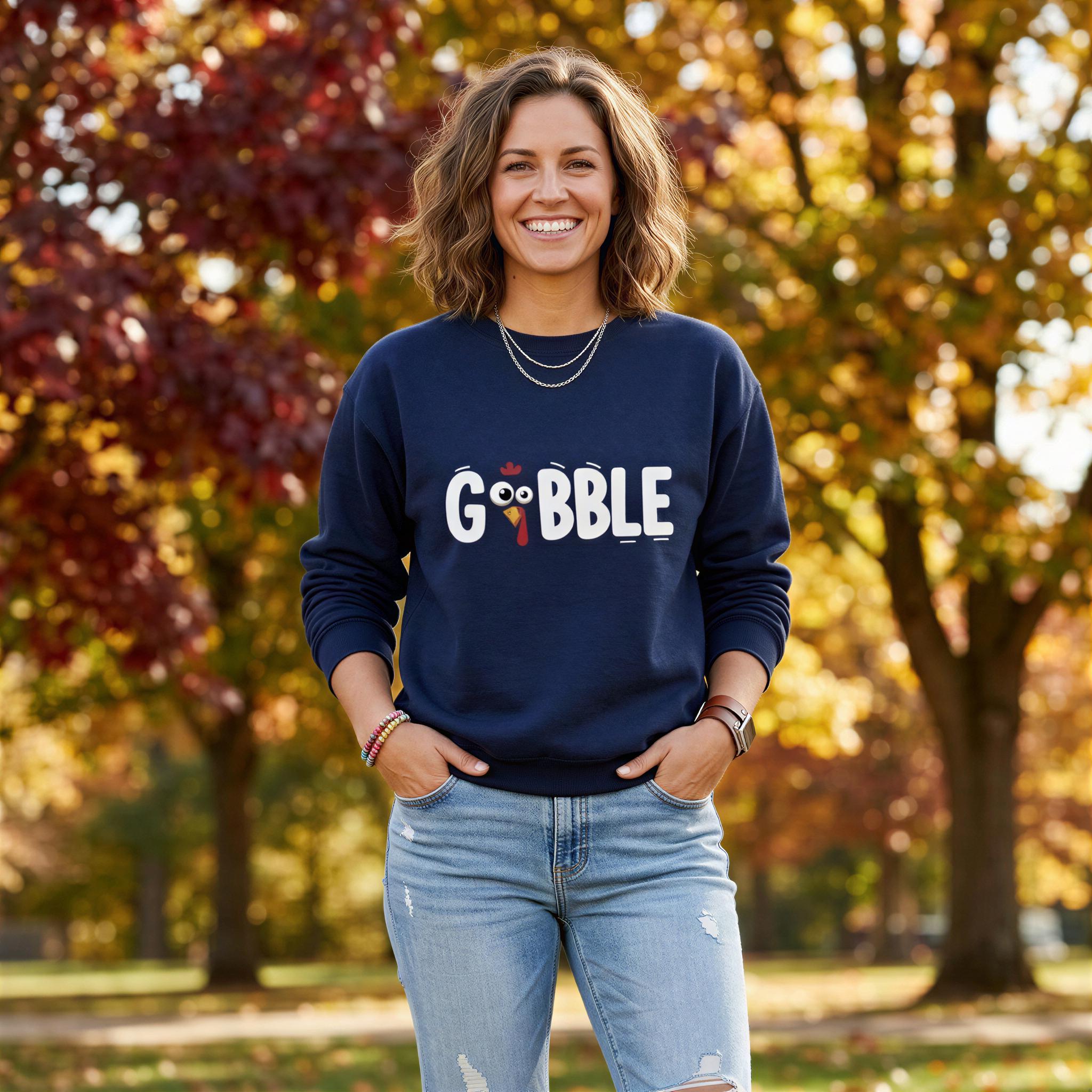 A woman wearing a navy blue sweatshirt with the word "GOBBLE" printed on it, standing in a park with autumn trees in the background.