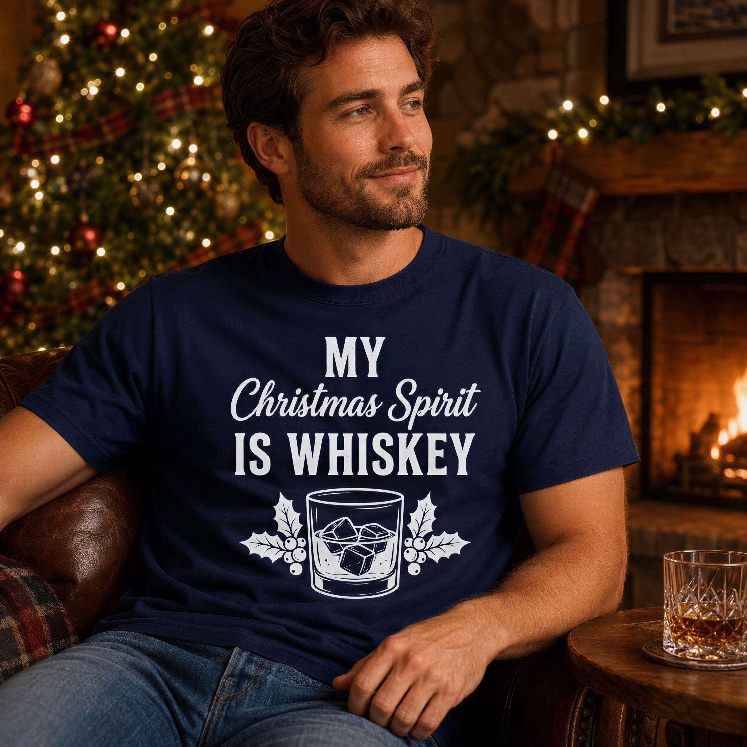 A man wearing a navy blue t-shirt with the text "MY CHRISTMAS SPIRIT IS WHISKEY" is sitting in a cozy living room with a fireplace and Christmas decorations in the background.