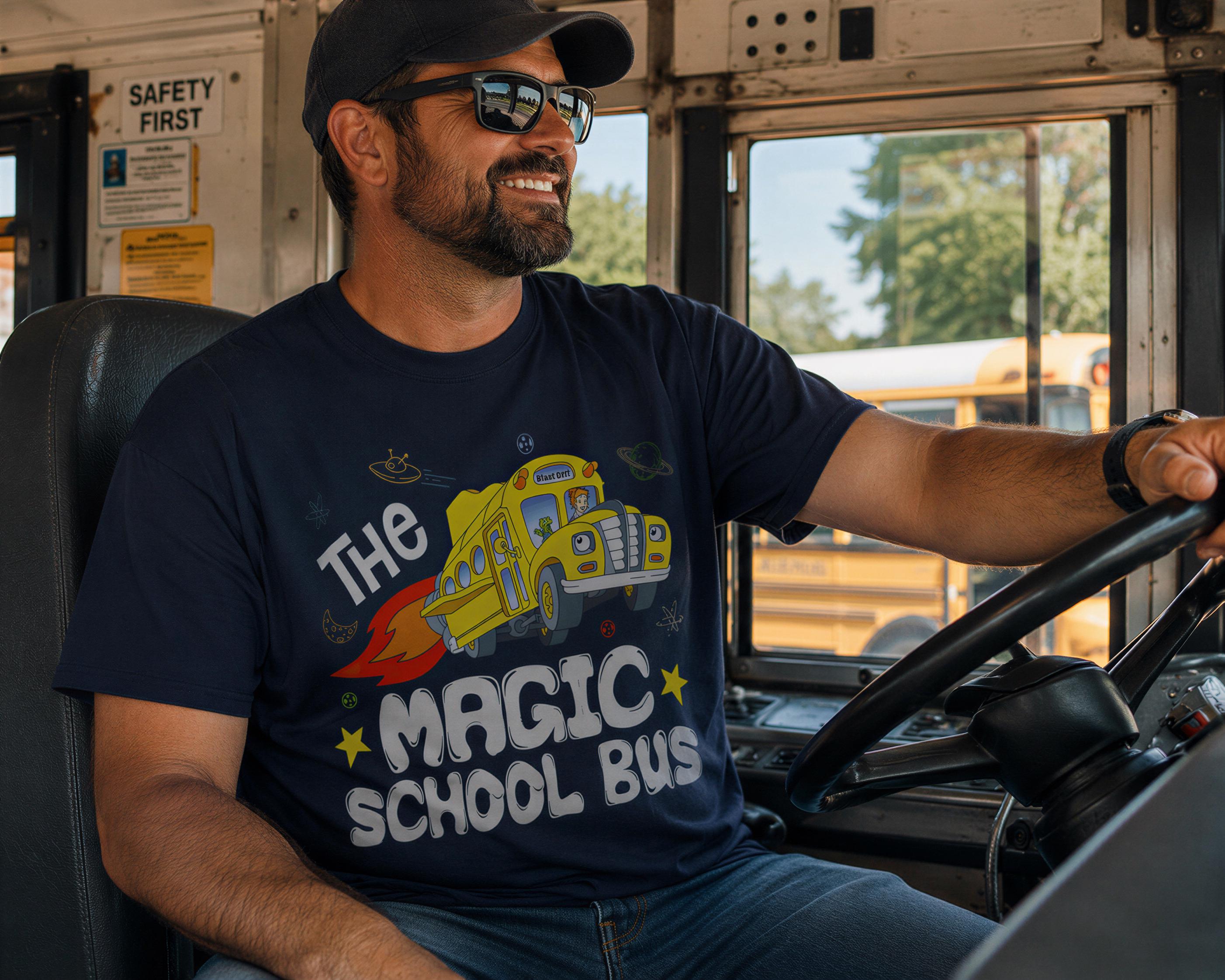 A man wearing a blue t-shirt with a graphic of a school bus and the text "The Magic School Bus" is sitting in the driver's seat of a school bus.