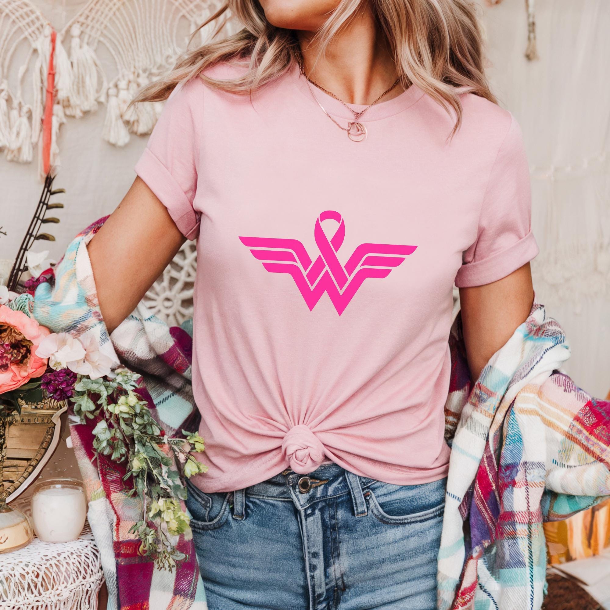 A woman wearing a pink t-shirt with a pink ribbon design stands in front of a floral backdrop.
