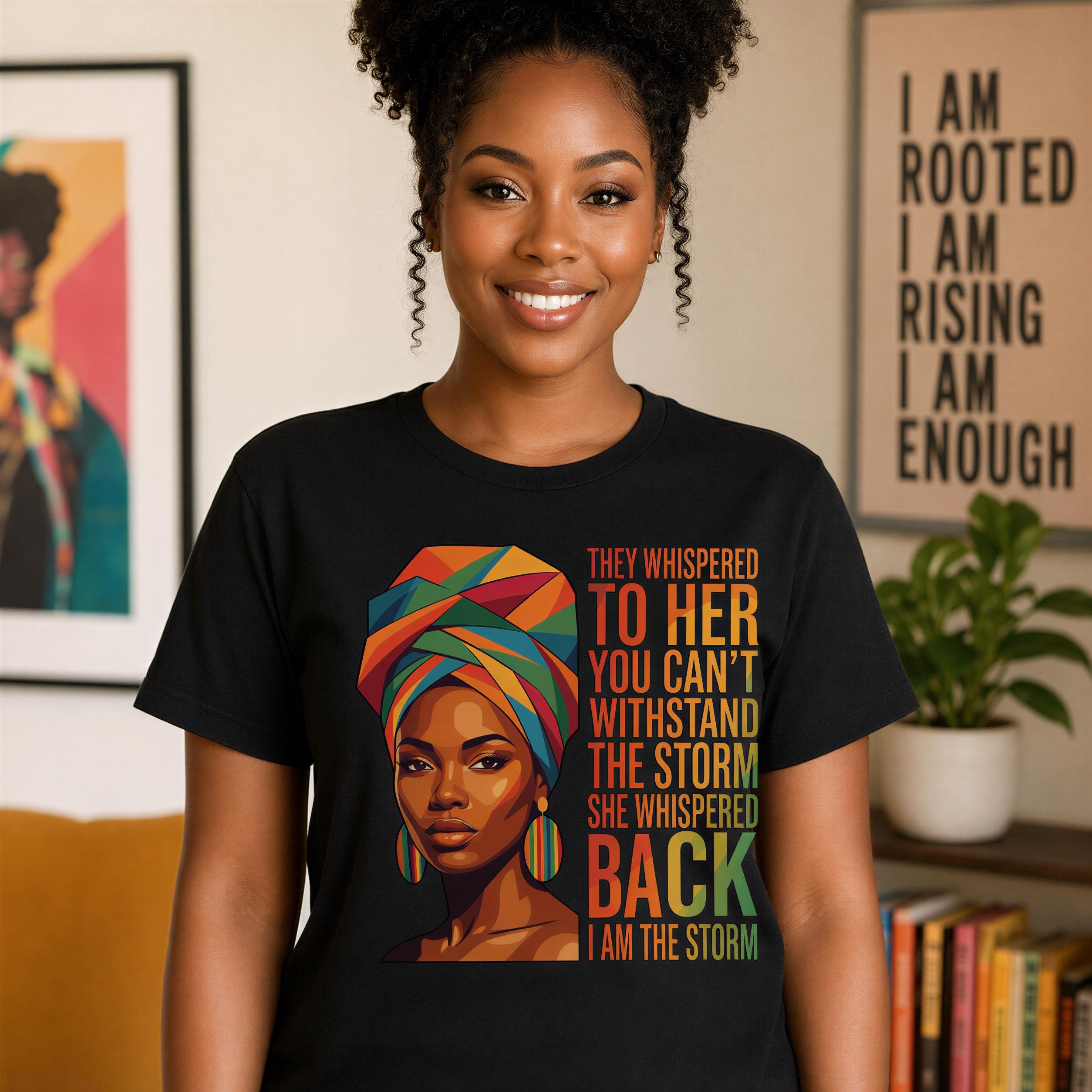 A woman wearing a black t-shirt with a colorful graphic of a woman's face and text that reads "They whispered to her you can't withstand the storm she whispered back I am the storm".