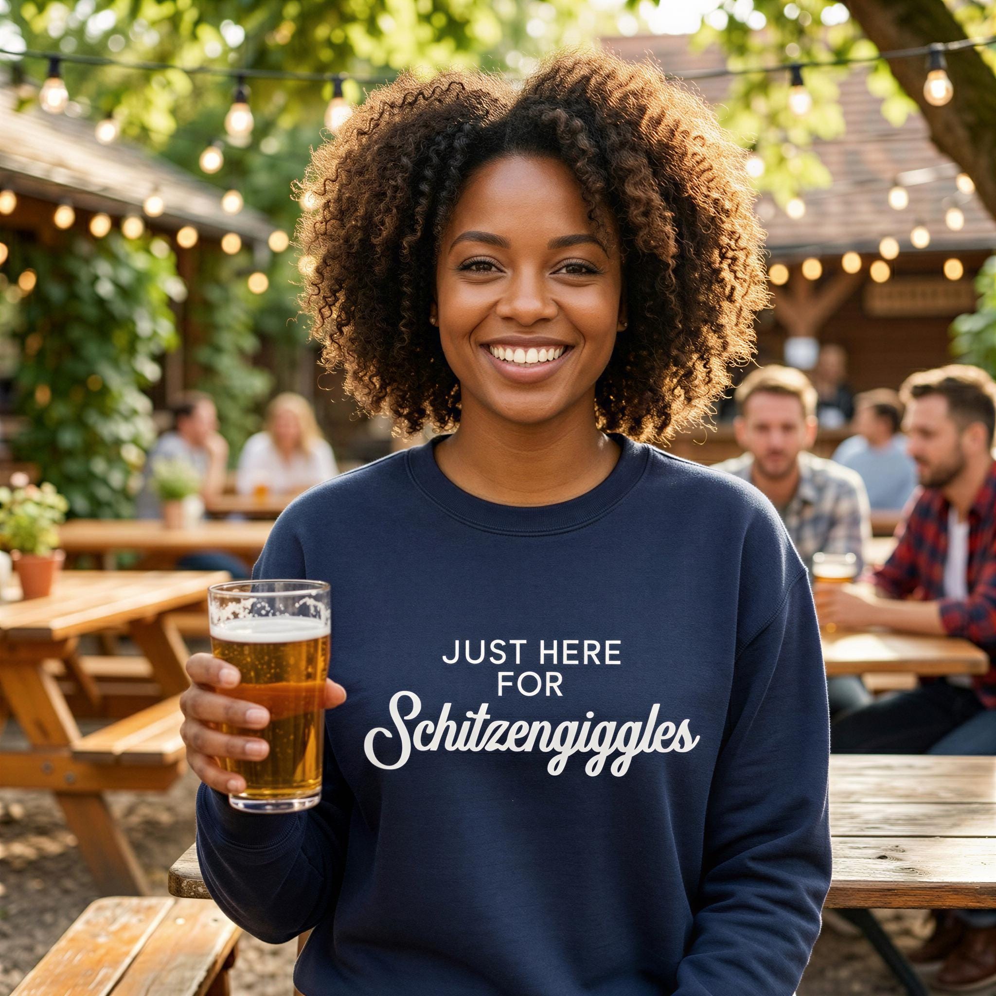 A smiling woman with curly hair is holding a glass of beer and wearing a blue sweatshirt with the text "Just here for Schitzangggles" printed on it.