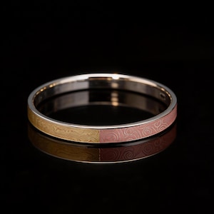 May include: A gold and pink bangle bracelet. The bracelet is split into two sections: one with a wood grain pattern in gold and the other with a swirl pattern in pink. The bracelet is set against a black background.